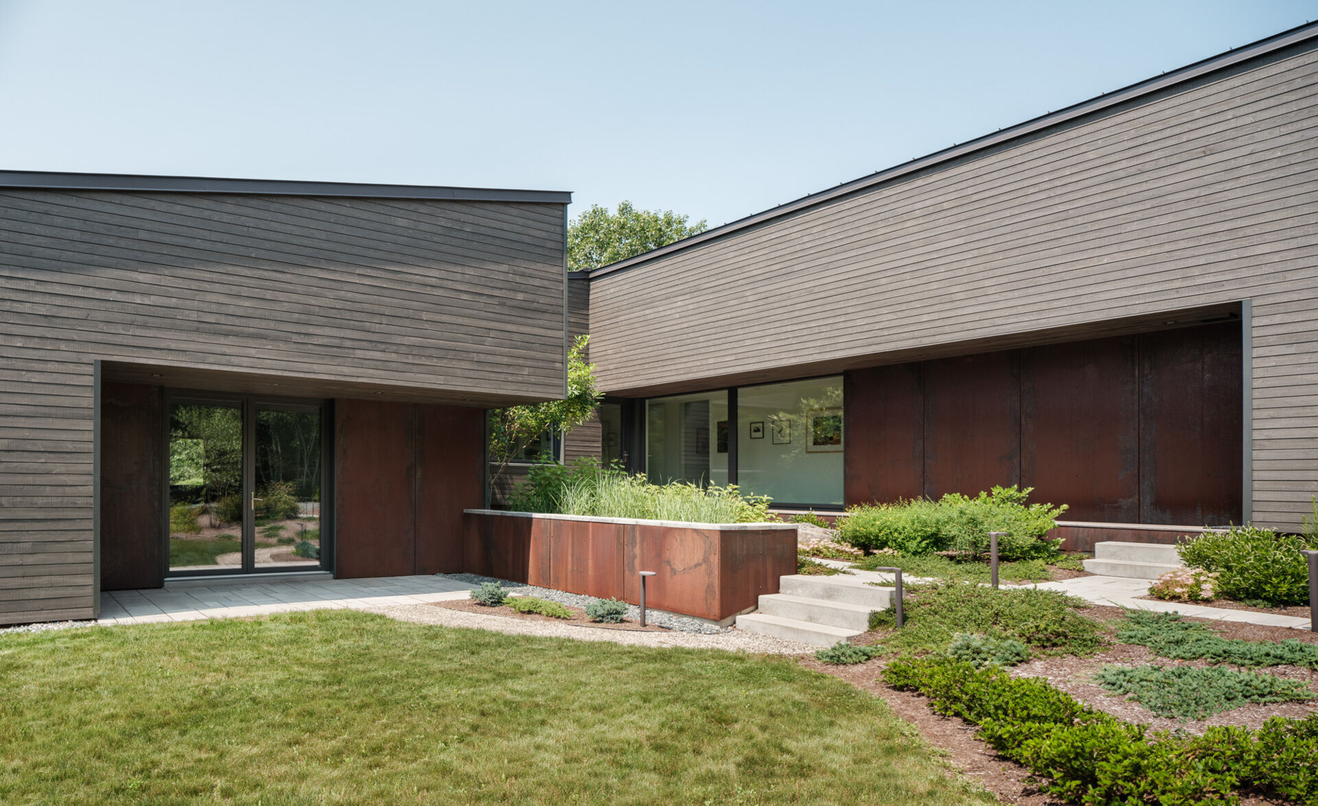 Stained cedar siding and Corten steel panels give this house a modern, grounded look that blends beautifully with the wooded riverside landscape.