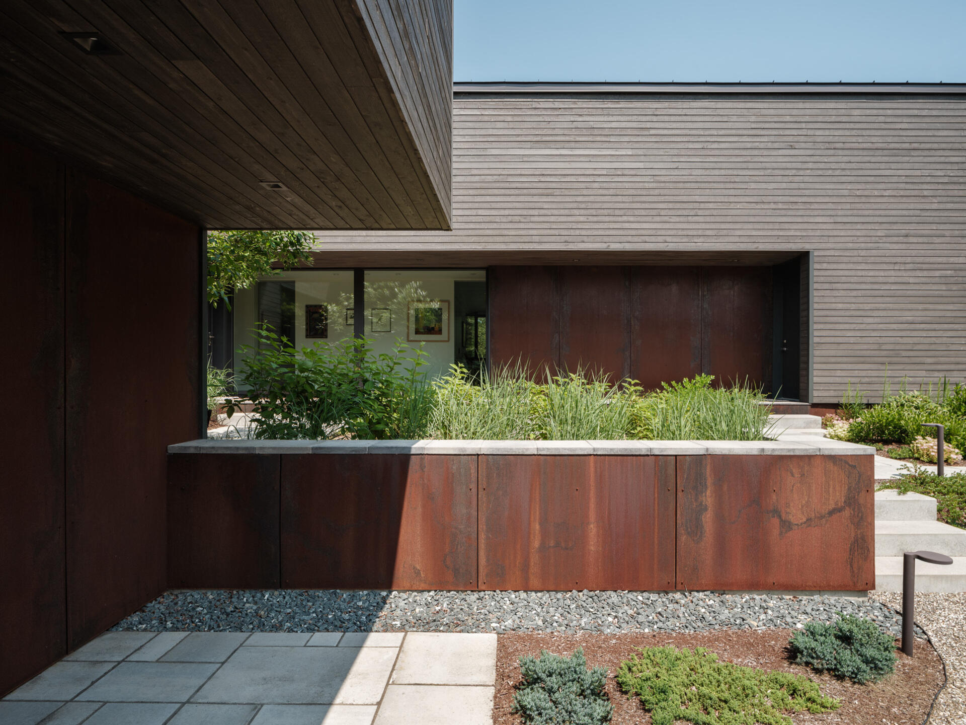 Stained cedar siding and Corten steel panels give this house a modern, grounded look that blends beautifully with the wooded riverside landscape.