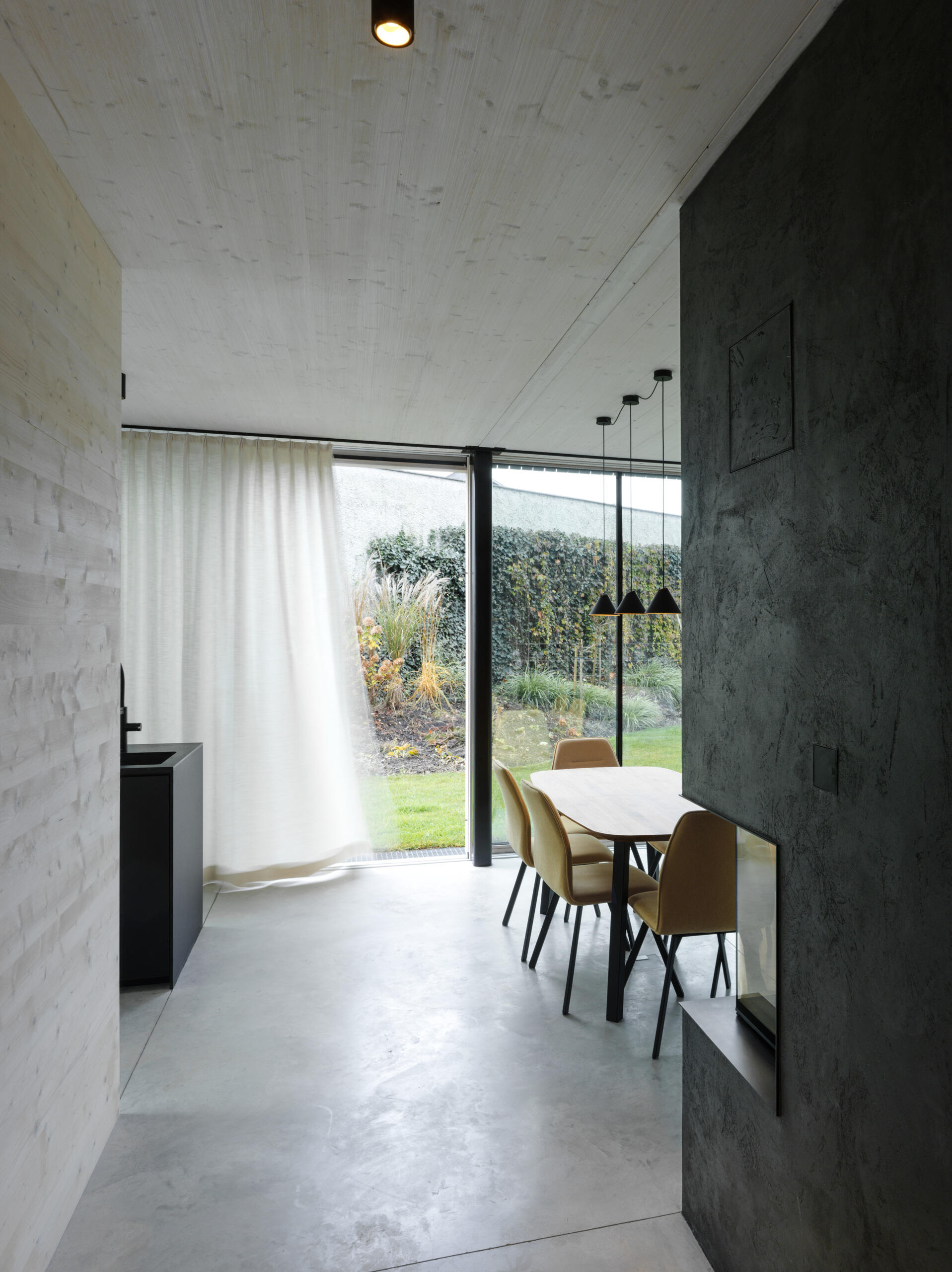 An open-plan ground floor with earthy materials and full-height glass doors connects the interior seamlessly to the garden.