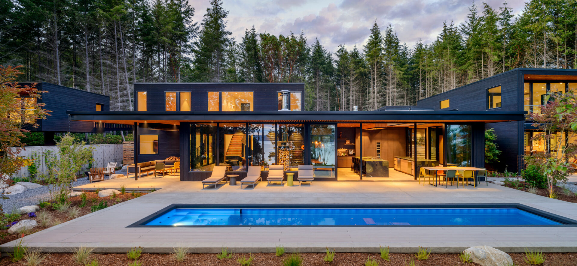 A forest-framed patio with a narrow lap pool, slatted ceiling, firepit, and warm wood details, designed for quiet mornings and slow evenings outdoors.