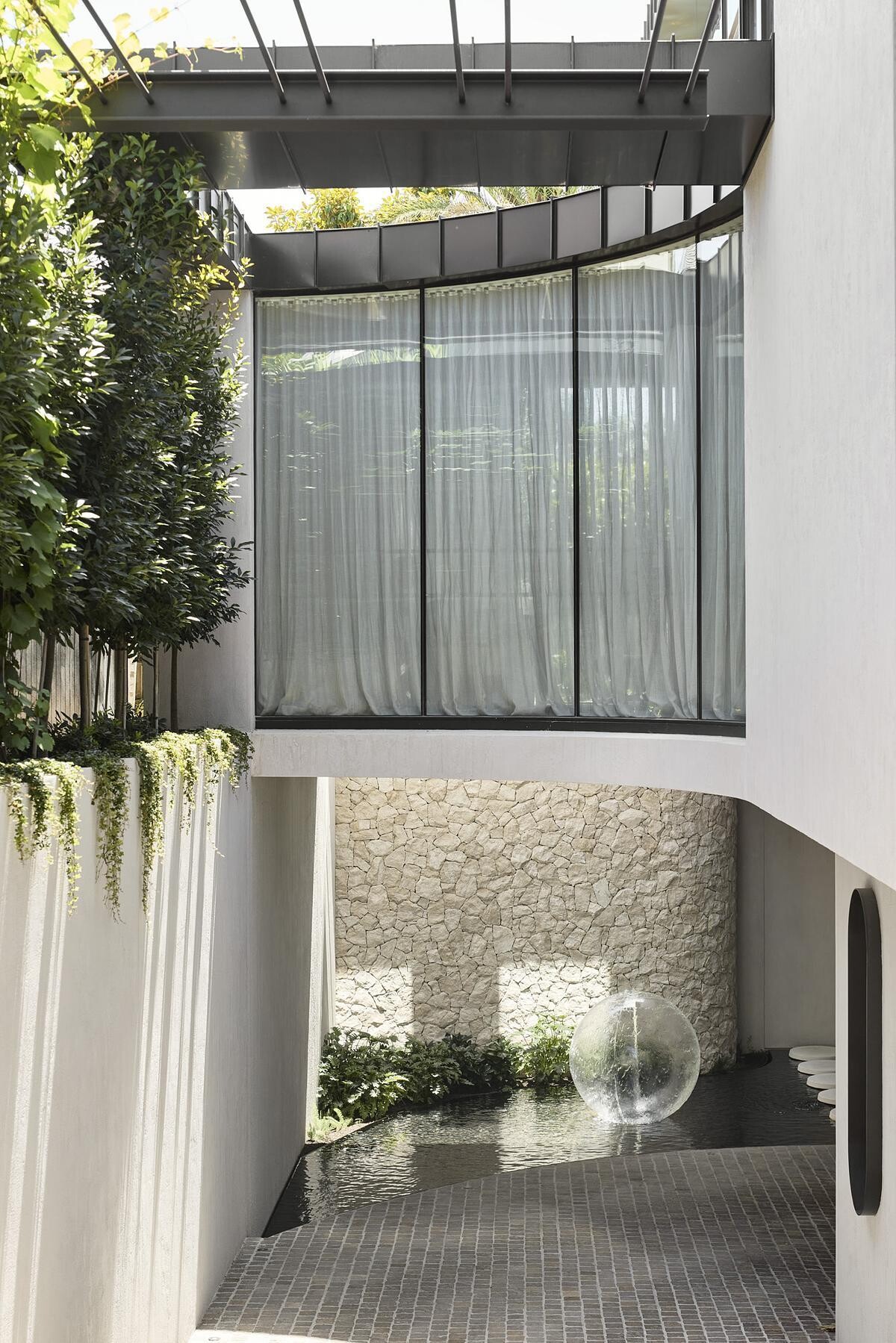 Natural rock cladding, curved forms, and expansive glazing define the sculptural exterior of this serene, modern Melbourne home.