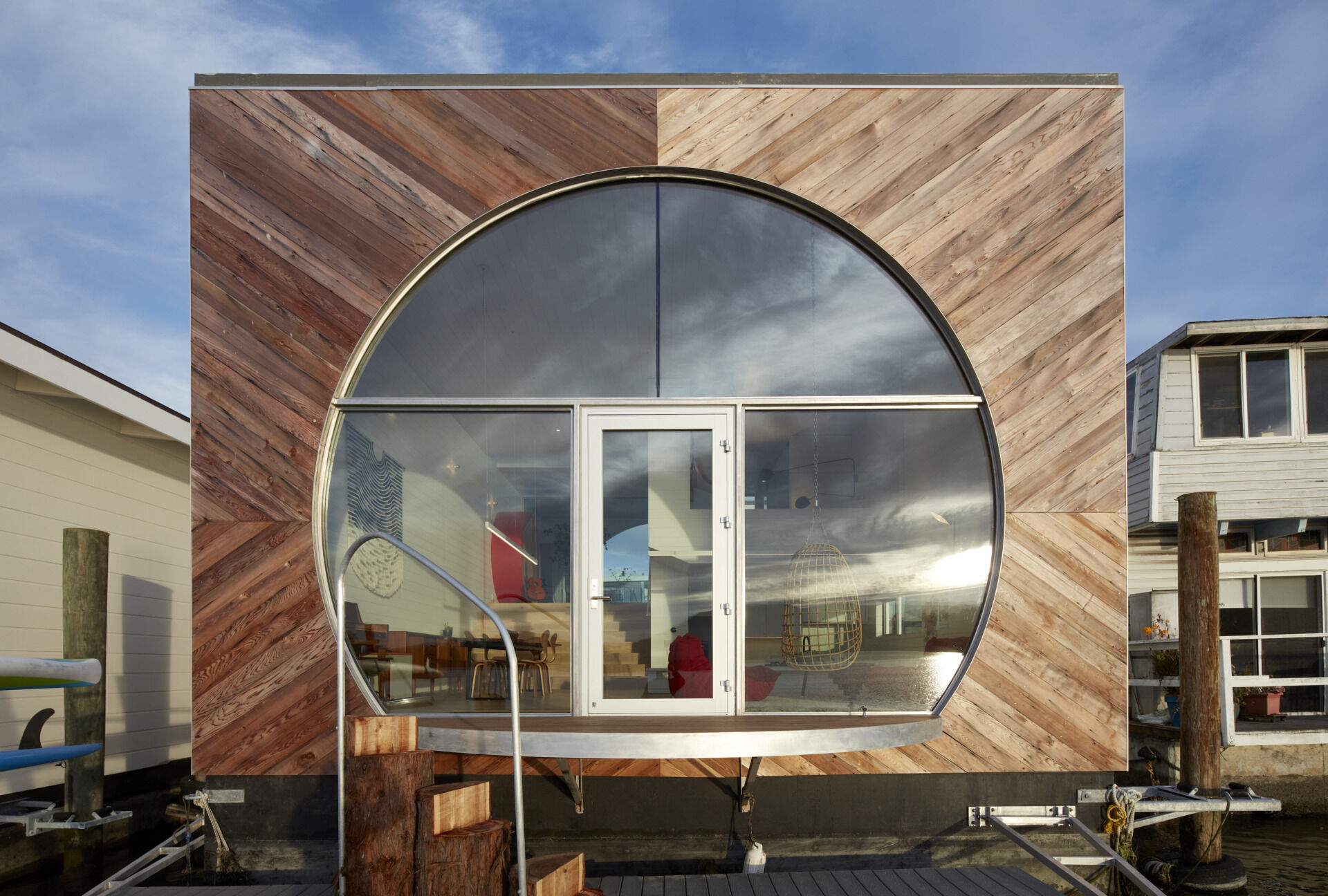 This modern houseboat showcases authentic waterfront living through its compact, efficient design. Featuring natural wood, weathered metal, and expansive glass, the layered structure blends seamlessly with its environment while honoring the community’s experimental roots.