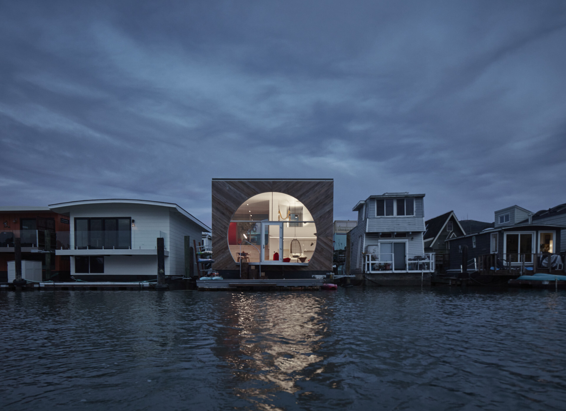 This modern houseboat showcases authentic waterfront living through its compact, efficient design. Featuring natural wood, weathered metal, and expansive glass, the layered structure blends seamlessly with its environment while honoring the community’s experimental roots.