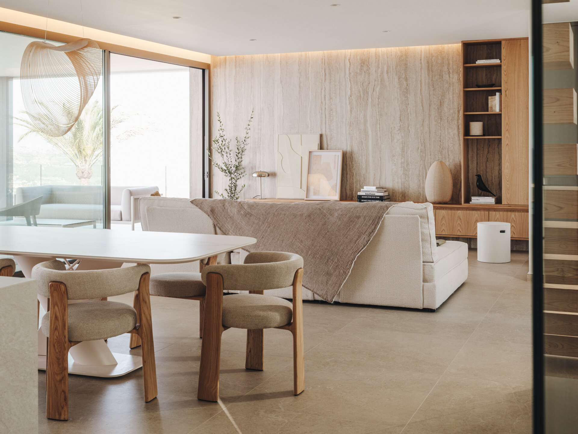 In this open plan dining area, a pale oak table and sculptural chairs sit beneath a soft pendant, framing views and continuing the home's natural palette.