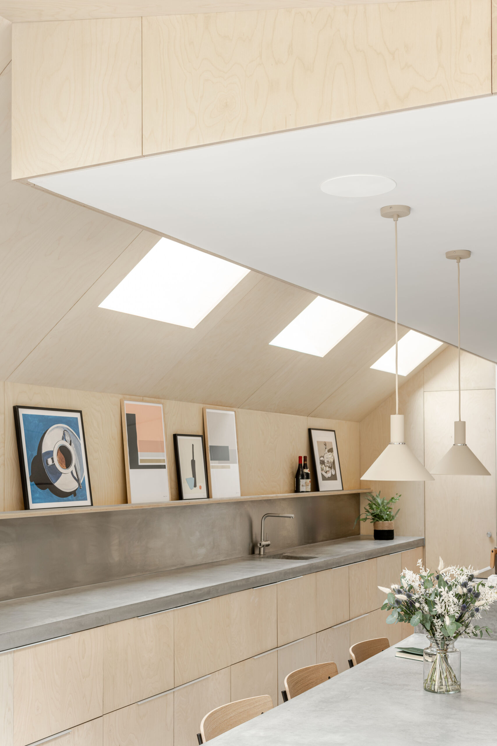Custom birch plywood cabinetry, a stainless steel backsplash, and soft concrete tones bring a quiet Scandinavian feel to this highly functional kitchen.