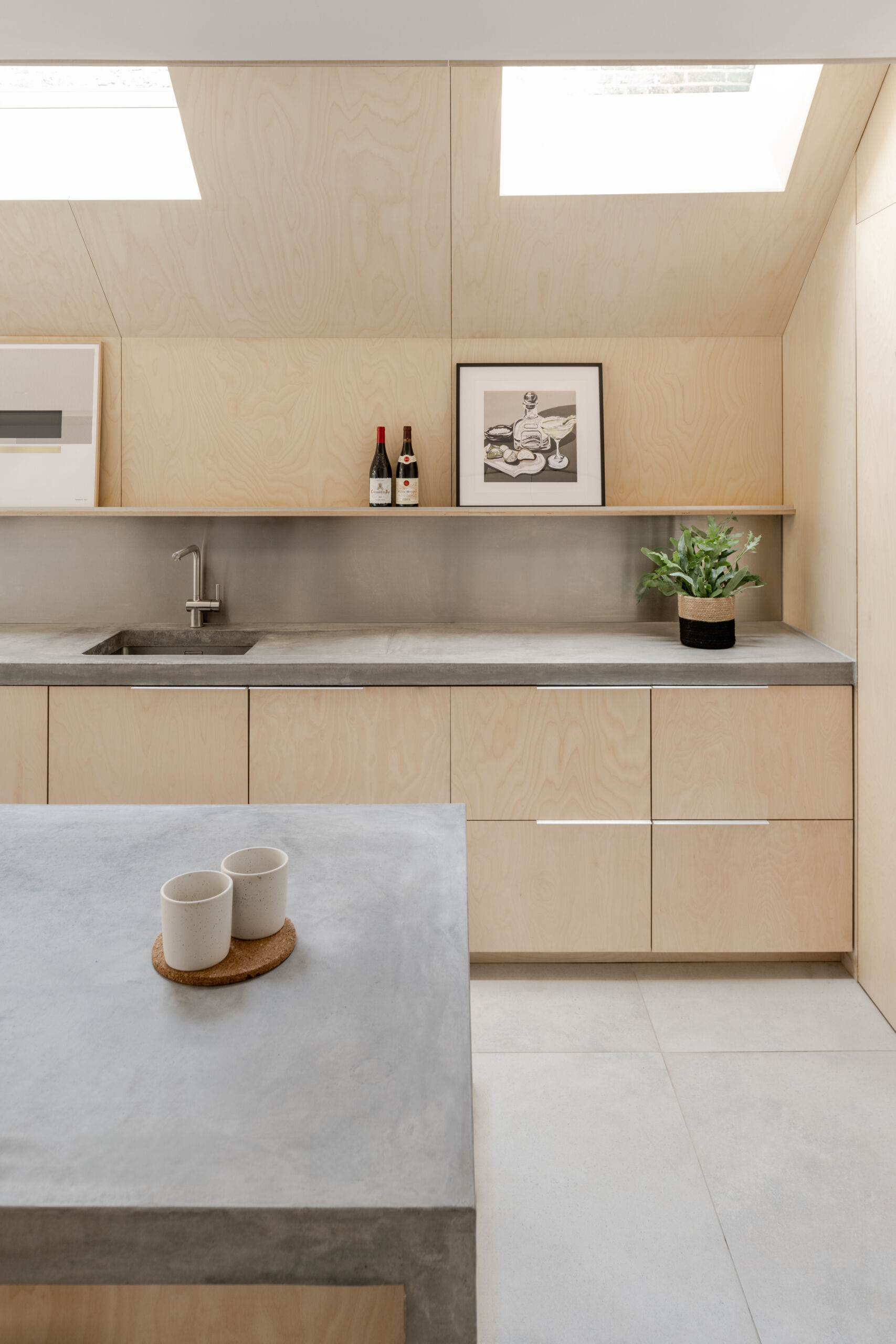 Custom birch plywood cabinetry, a stainless steel backsplash, and soft concrete tones bring a quiet Scandinavian feel to this highly functional kitchen.