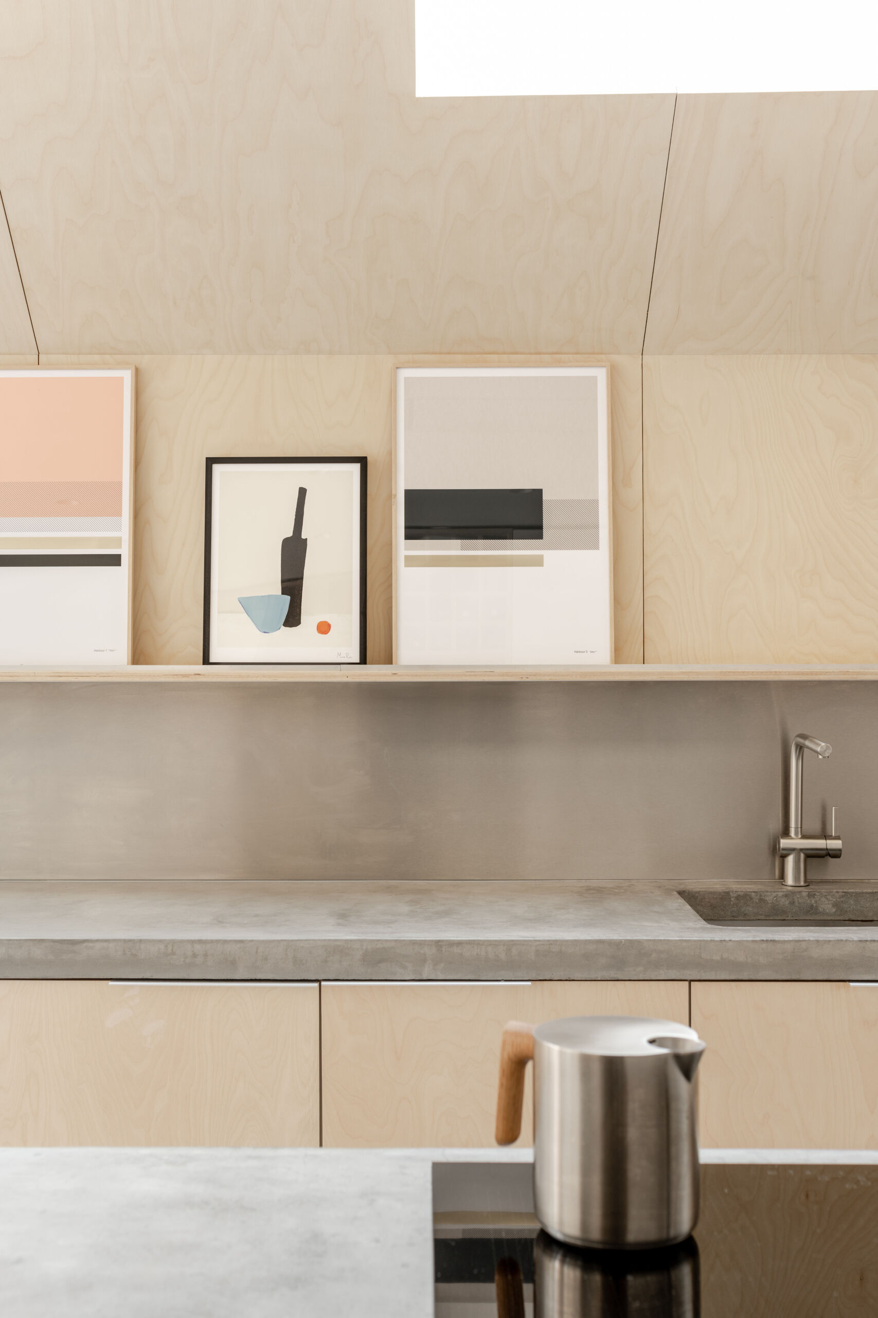 Custom birch plywood cabinetry, a stainless steel backsplash, and soft concrete tones bring a quiet Scandinavian feel to this highly functional kitchen.