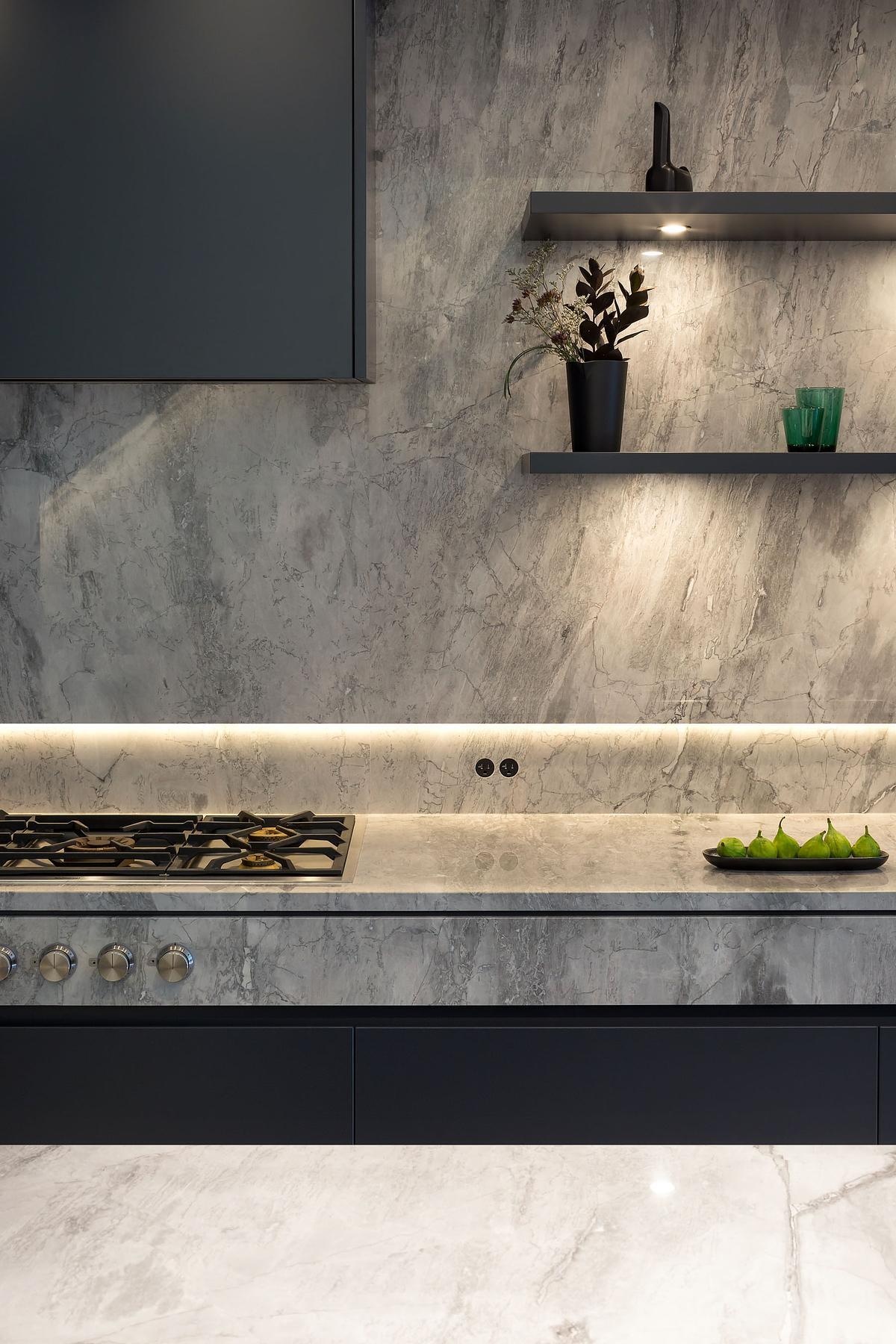 Black cabinetry, Gaggenau appliances, and marble counters give this kitchen a sculptural feel. The floating wood staircase beside it adds architectural drama.