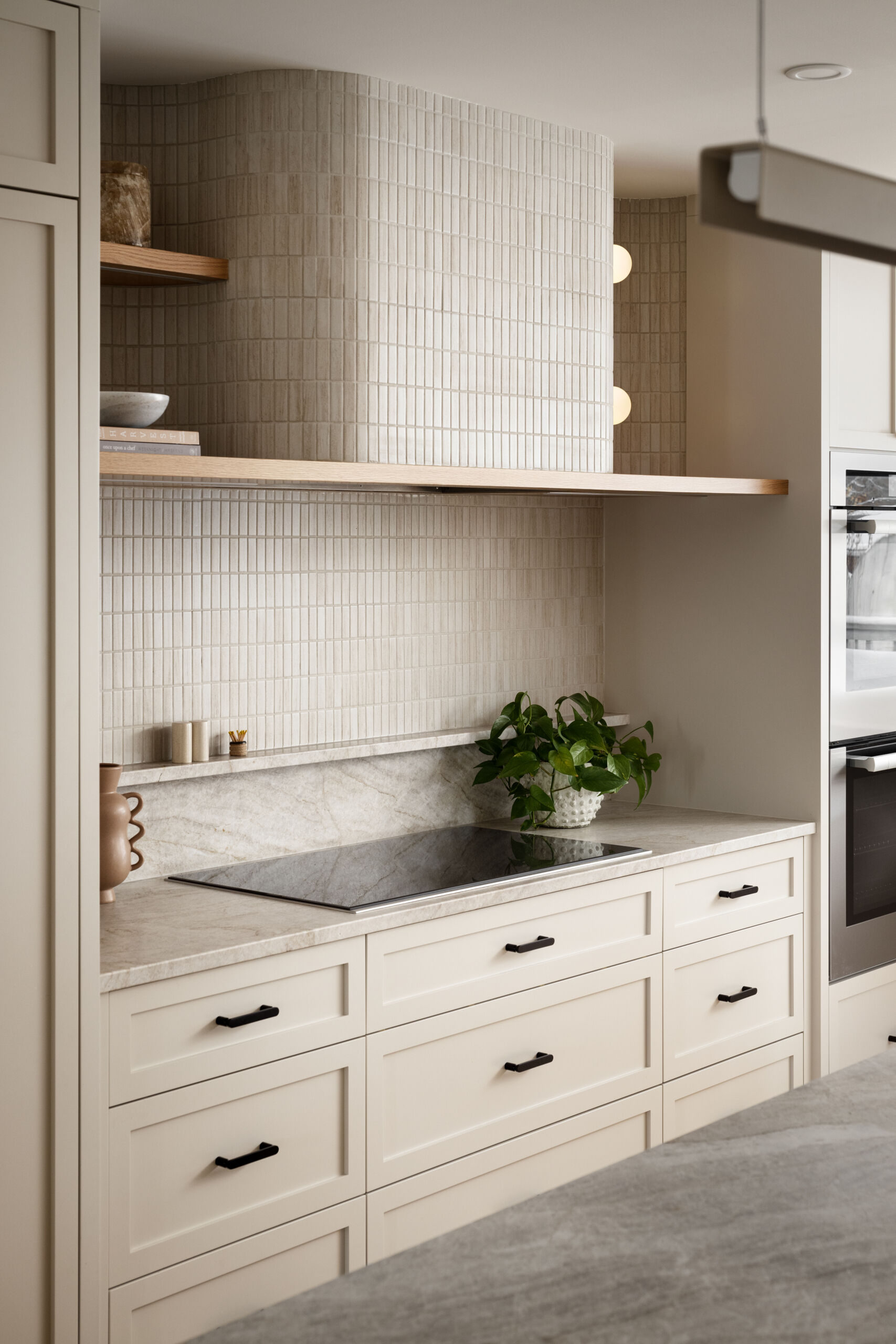 At the heart of this home lies the redesigned kitchen with neutral cabinetry and countertops to reflect light and stretch sightlines. A warm wood island blends into the hardwood flooring, encouraging a natural visual flow toward the rear windows. A curved hood fan and island counter softens the typical edges of kitchen details and continuing the home’s curvilinear language.