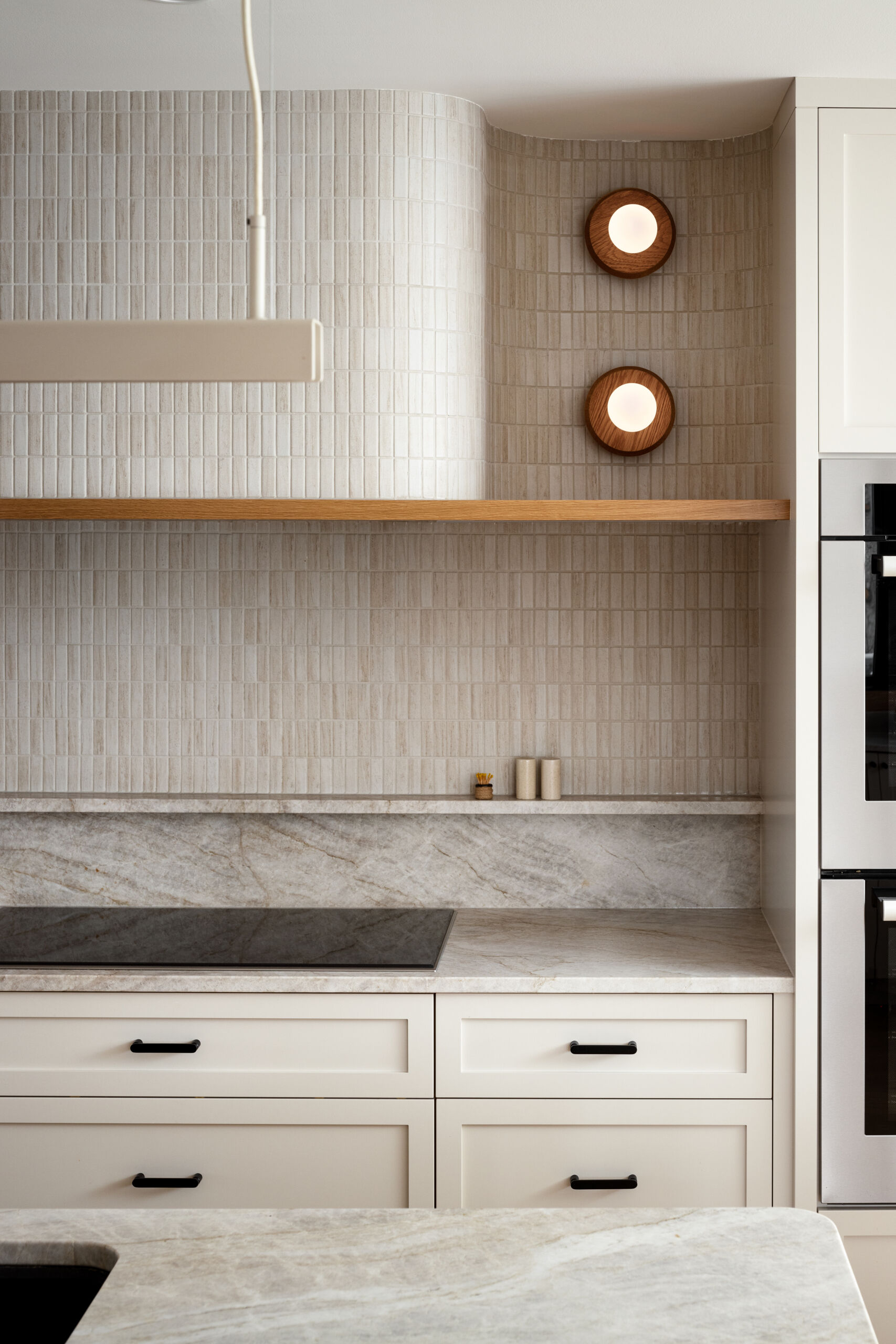At the heart of this home lies the redesigned kitchen with neutral cabinetry and countertops to reflect light and stretch sightlines. A warm wood island blends into the hardwood flooring, encouraging a natural visual flow toward the rear windows. A curved hood fan and island counter softens the typical edges of kitchen details and continuing the home’s curvilinear language.