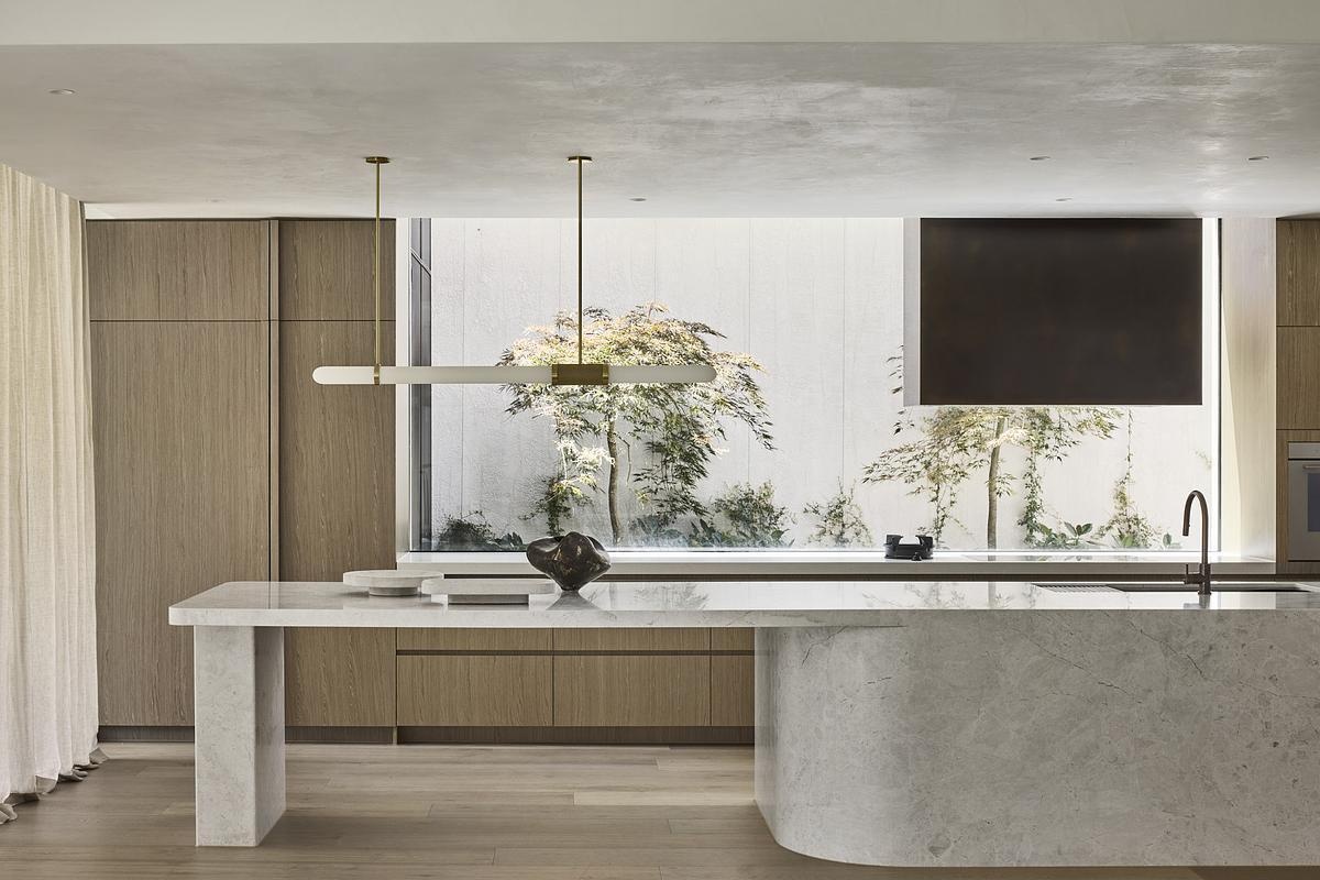 A marble island, pale timber cabinetry, and garden views make this minimalist kitchen feel effortlessly luxurious and serene.
