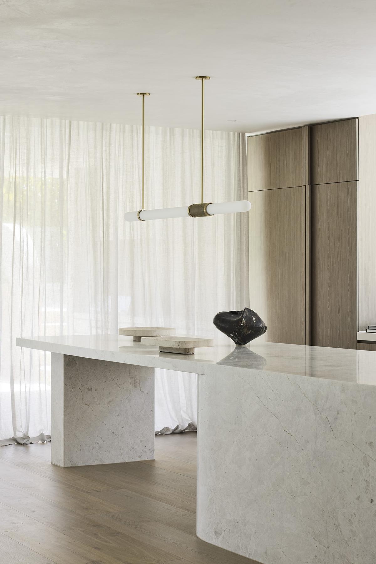 A marble island, pale timber cabinetry, and garden views make this minimalist kitchen feel effortlessly luxurious and serene.
