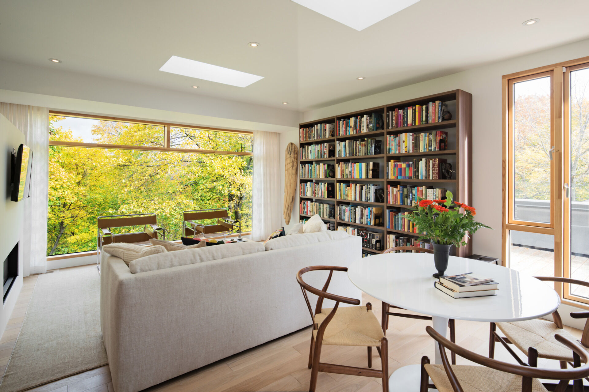 The upper-level study is a peaceful retreat with a large picture window framing ravine views. Featuring cozy bookshelves, a round table, and access to a rooftop deck, it blends comfort with nature.