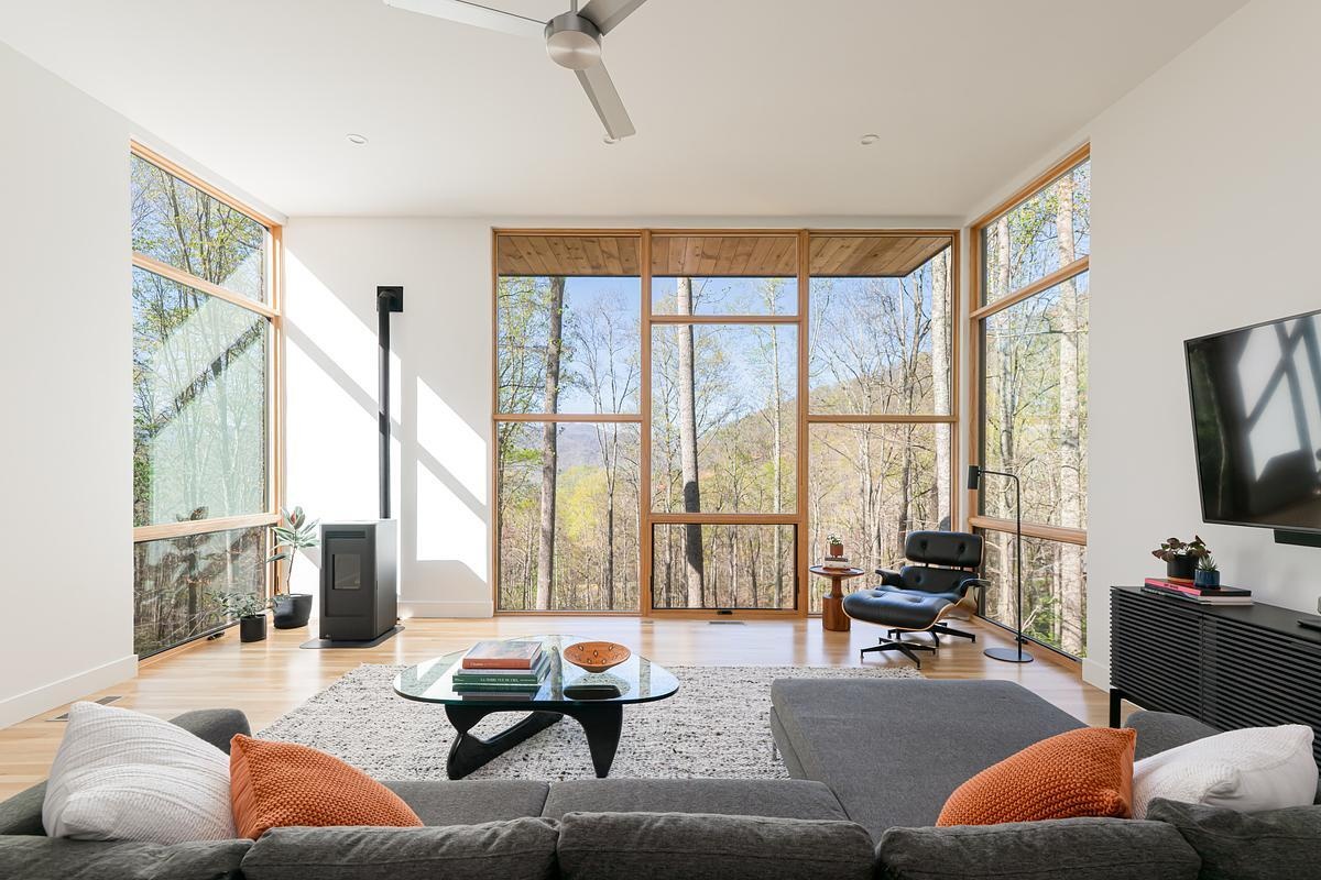 The living room is the heart of the home, designed as a bright sanctuary where views of the forest and valley take center stage. Large windows frame the changing seasons and shifting light, making it feel like a treehouse suspended above the landscape. The clean lines and open plan foster both relaxation and contemplation.