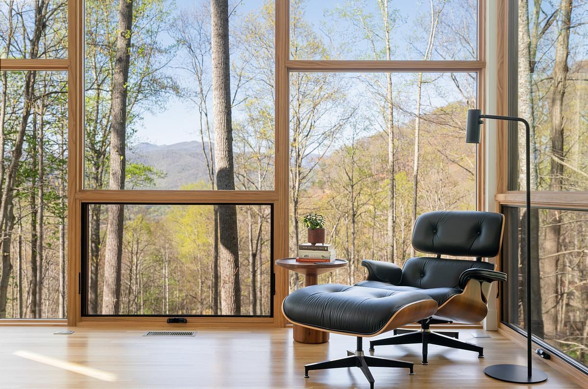 The living room is the heart of the home, designed as a bright sanctuary where views of the forest and valley take center stage. Large windows frame the changing seasons and shifting light, making it feel like a treehouse suspended above the landscape. The clean lines and open plan foster both relaxation and contemplation.