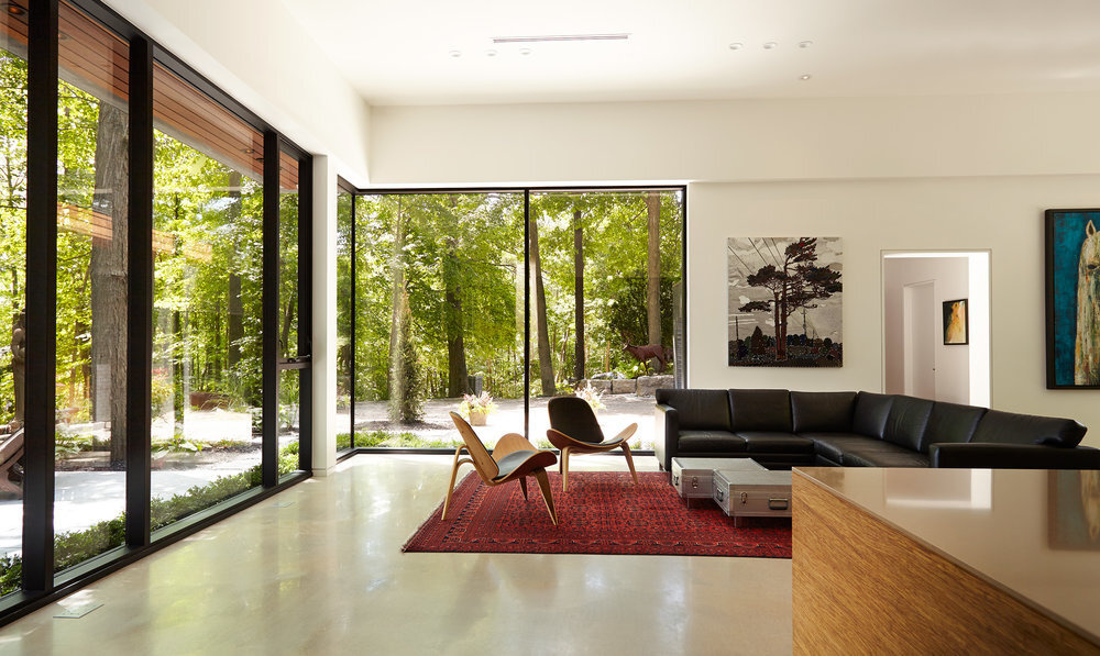 This living area is bright and serene, with white walls that frame leafy glimpses of the surrounding forest. It’s a space designed for stillness and reflection, where light shifts throughout the day and nature feels just a glance away.
