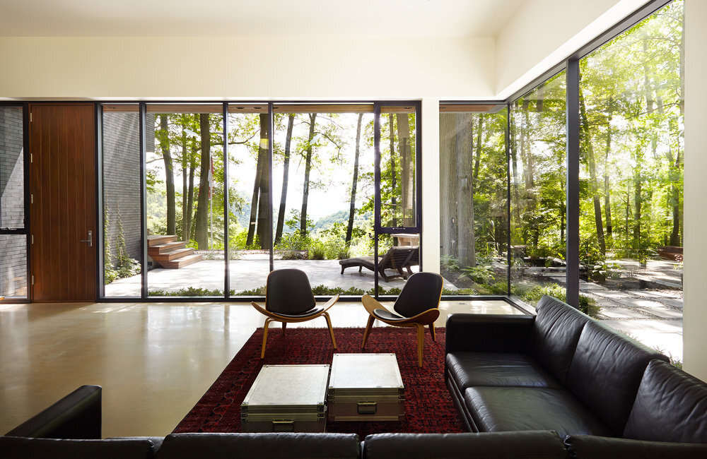 This living area is bright and serene, with white walls that frame leafy glimpses of the surrounding forest. It’s a space designed for stillness and reflection, where light shifts throughout the day and nature feels just a glance away.