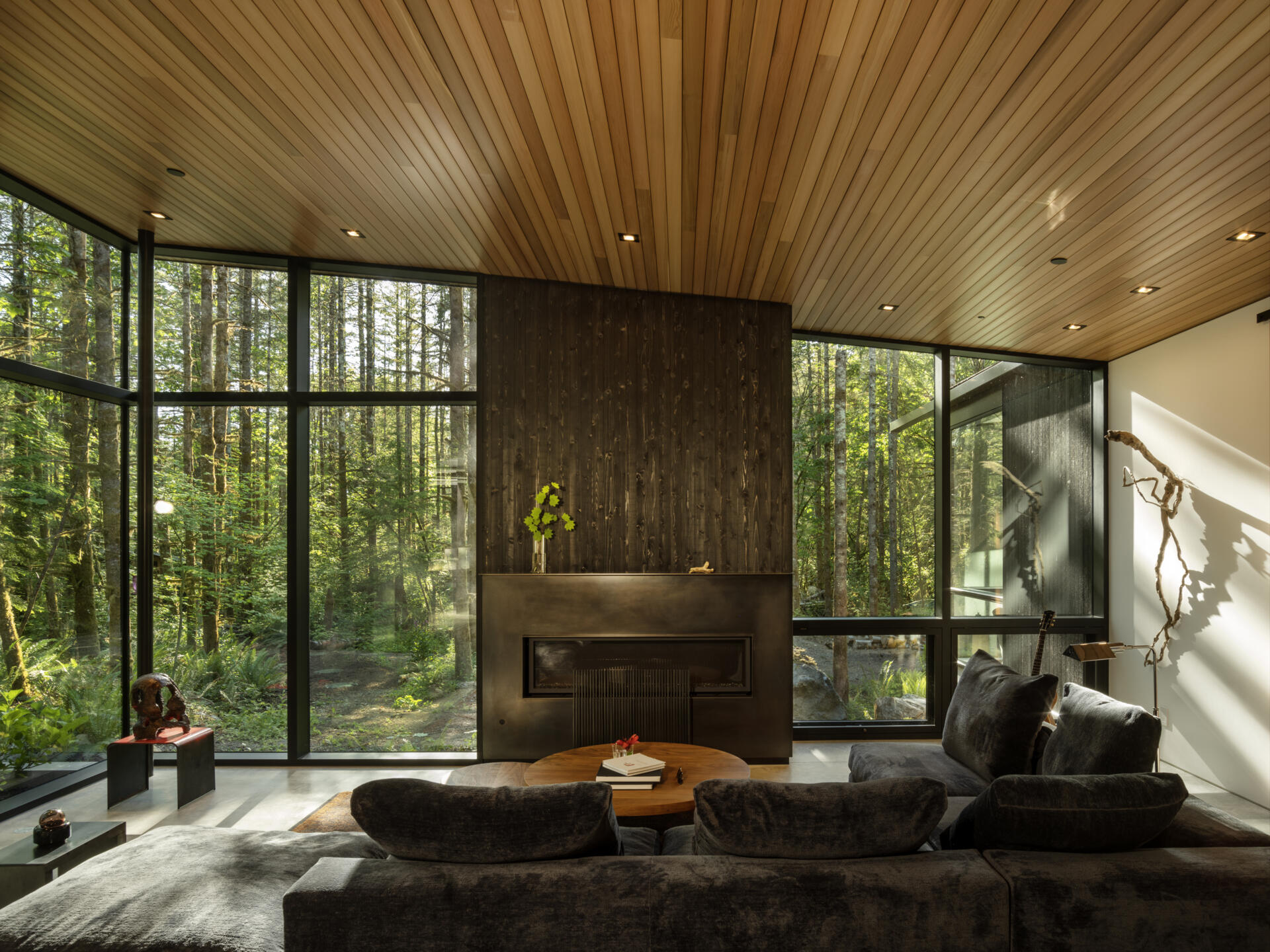The living room prioritizes views with expanses of windows, and seating oriented toward the fireplace with its steel surround, rather than a screen. Daylight shifts through the space, tracing the sun’s path, bringing softness and warmth to this otherwise rain-heavy region.