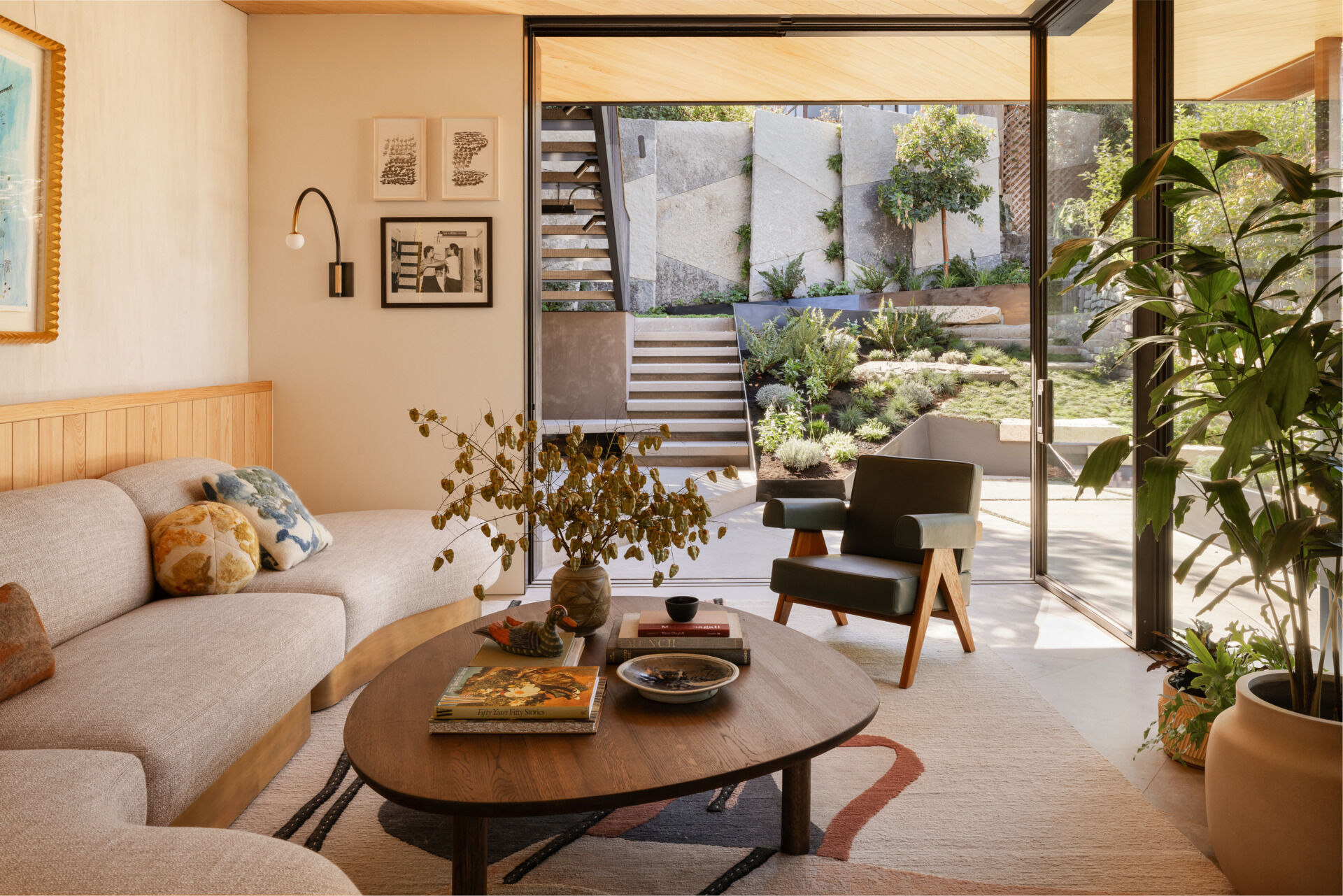 This sunlit living room features a Coup d'Etat sofa and rug by Fay Toogood, that ground the space with layered texture, while an Allied Maker sconce adds sculptural warmth. Just outside, the patio extends the room’s footprint, creating an easy connection to the outdoors.
