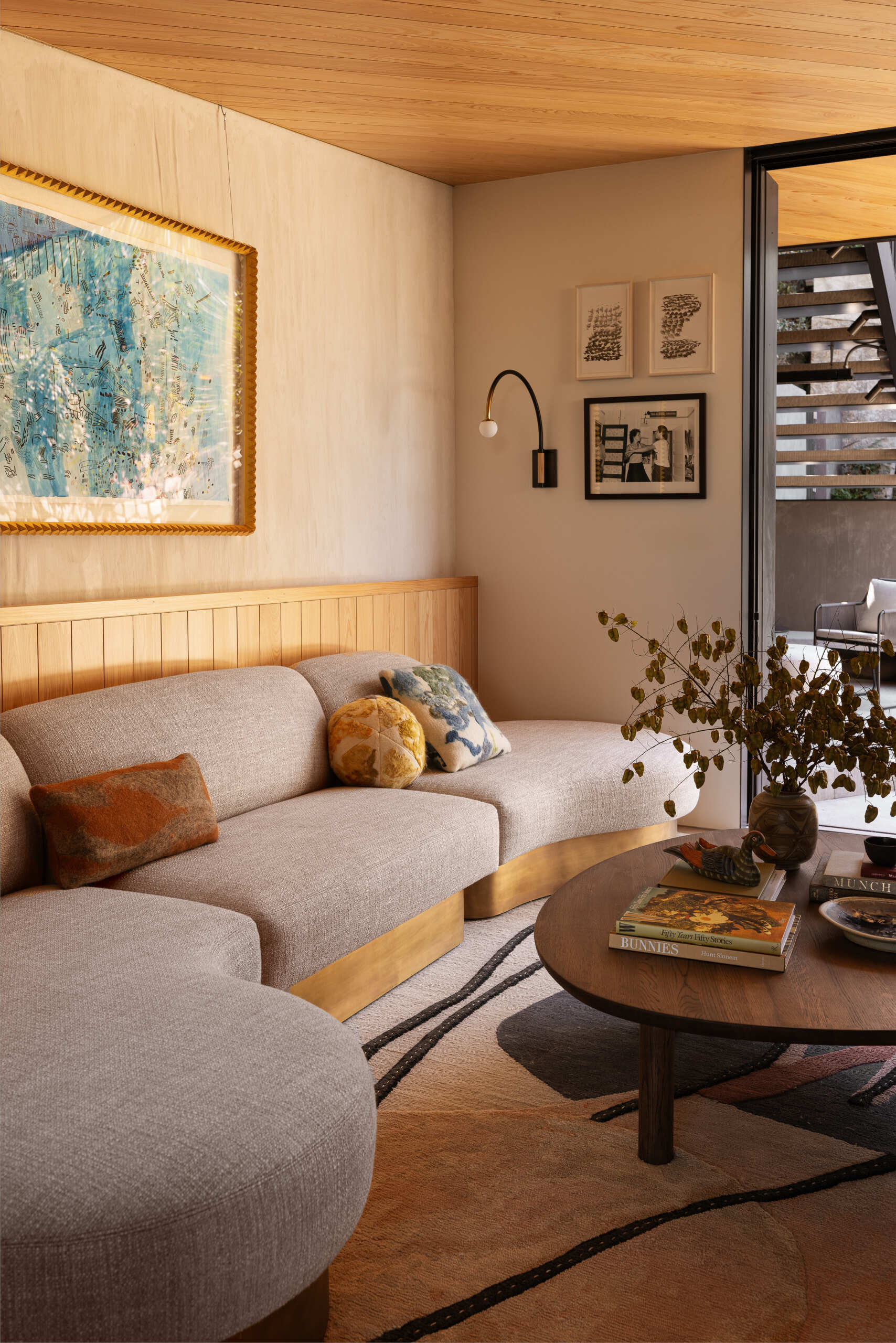This sunlit living room features a Coup d'Etat sofa and rug by Fay Toogood, that ground the space with layered texture, while an Allied Maker sconce adds sculptural warmth. Just outside, the patio extends the room’s footprint, creating an easy connection to the outdoors.