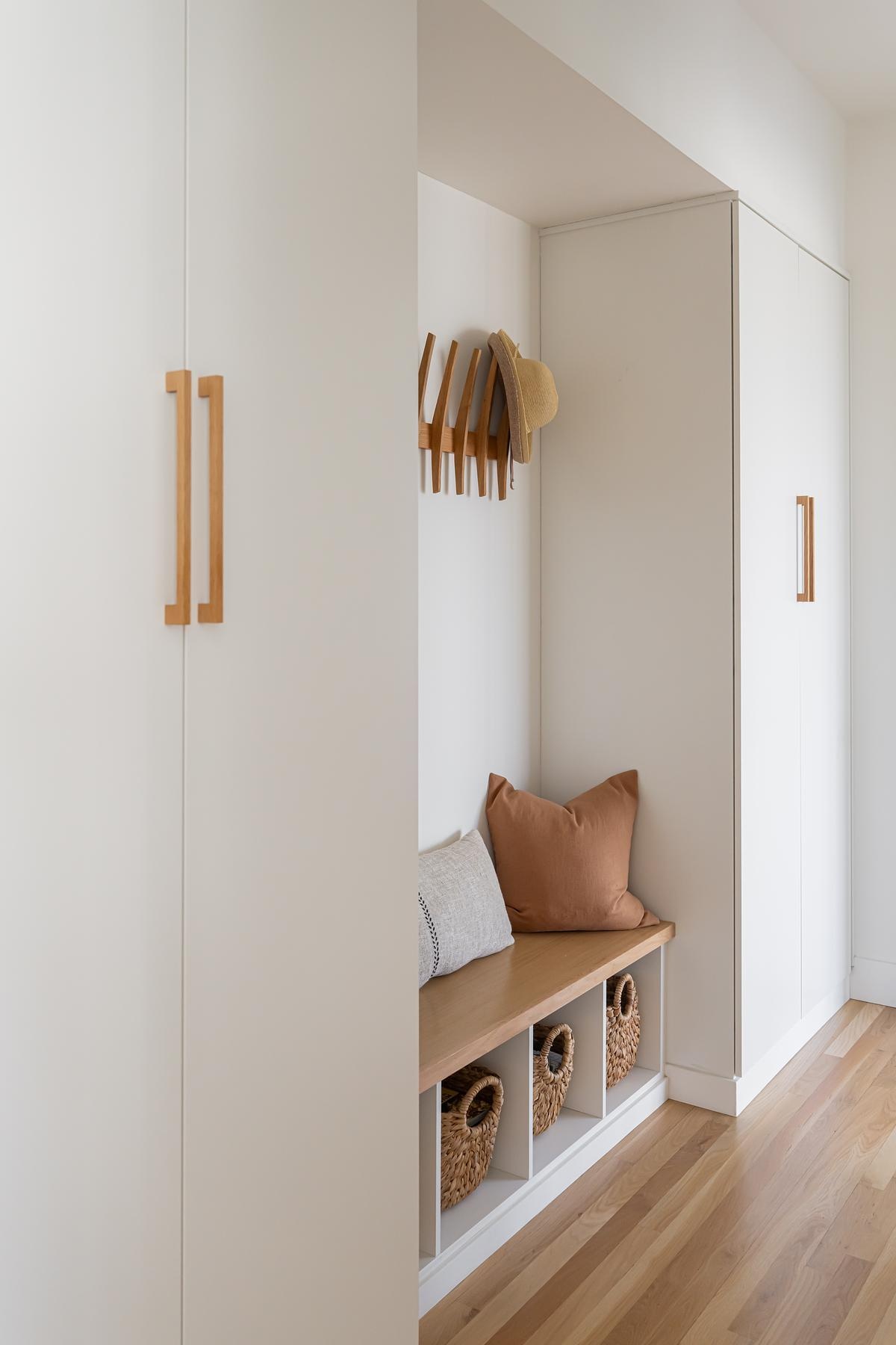 Off to the side of the front door and down a small hallway, a simple bench provides a practical spot to sit or remove shoes, with built-in storage to keep the space clutter-free. This understated feature supports the home’s clean, minimal aesthetic while addressing everyday needs with quiet efficiency.
