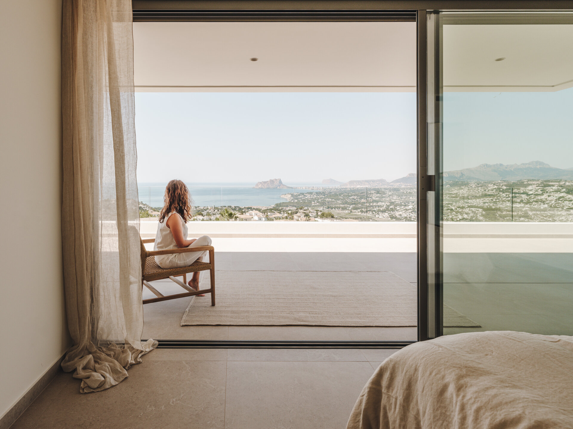 A serene upper-floor bedroom retreat where oak and travertine combine with filtered light and horizon-facing views.