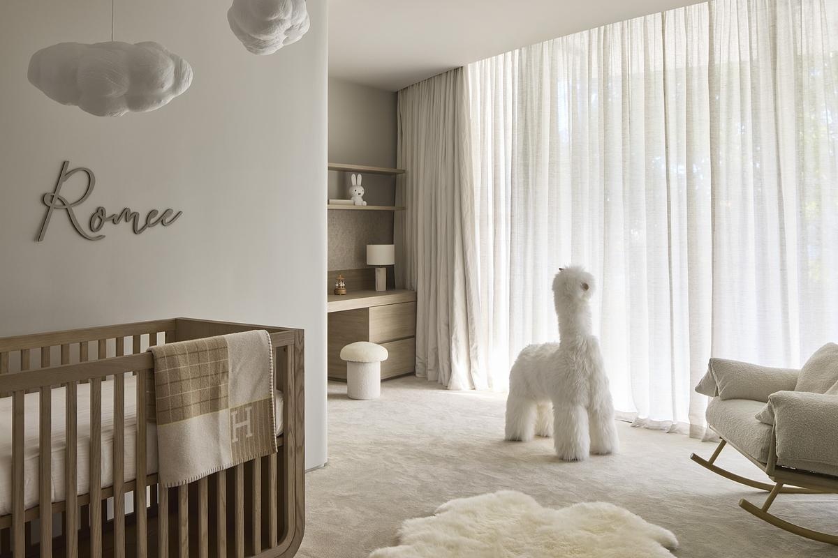 Soft light drifts through sheer curtains in the serene nursery, where gentle textures and rounded shapes create a calming atmosphere. The curved wooden crib brings warmth and stability, while cloud-like mobiles and a playful llama spark a quiet sense of magic.