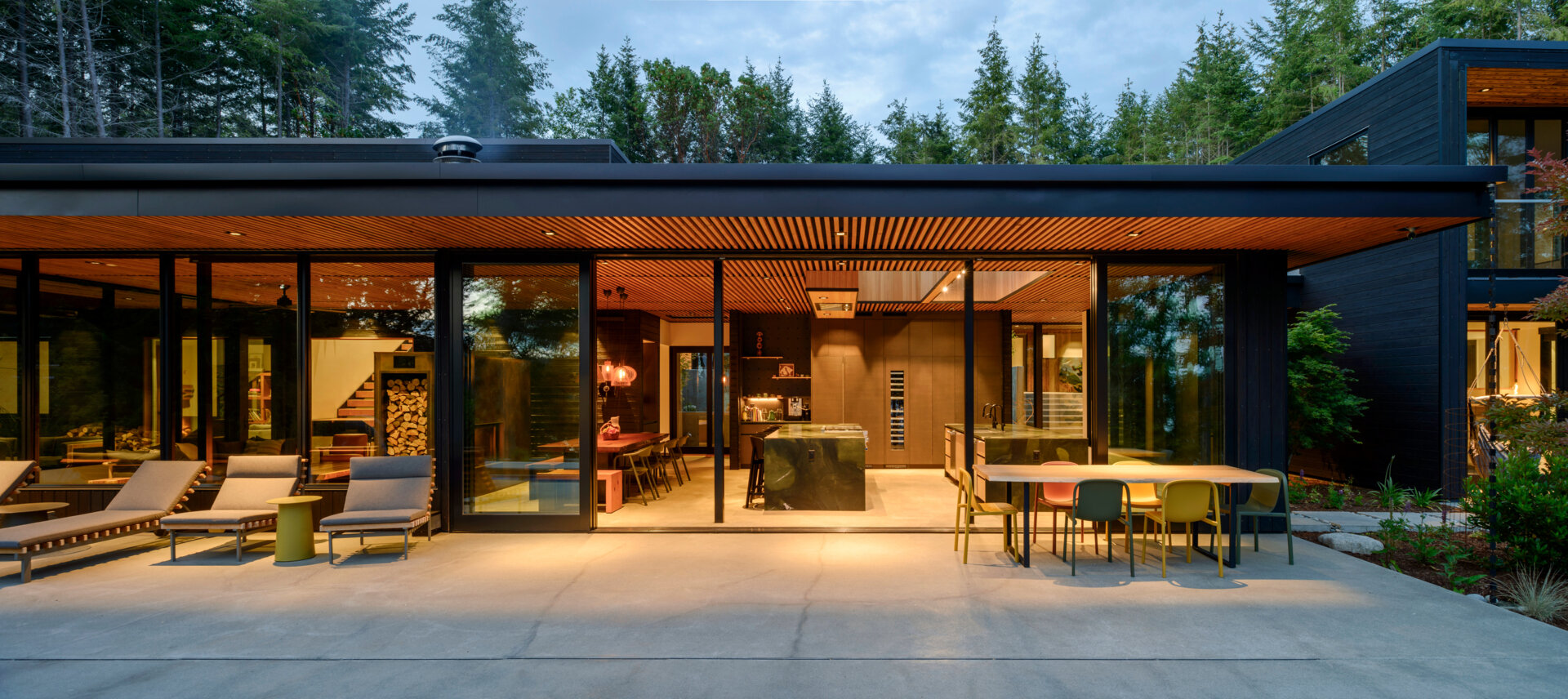 A forest-framed patio with a narrow lap pool, slatted ceiling, firepit, and warm wood details, designed for quiet mornings and slow evenings outdoors.