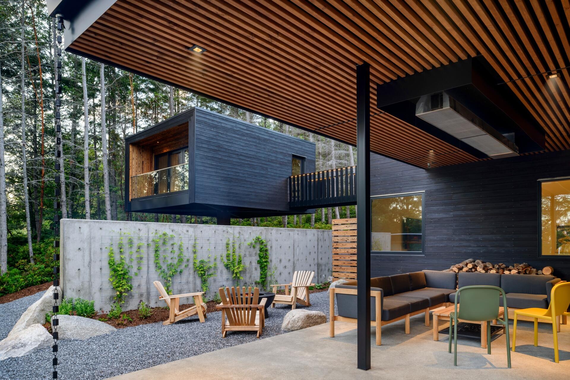 A forest-framed patio with a narrow lap pool, slatted ceiling, firepit, and warm wood details, designed for quiet mornings and slow evenings outdoors.