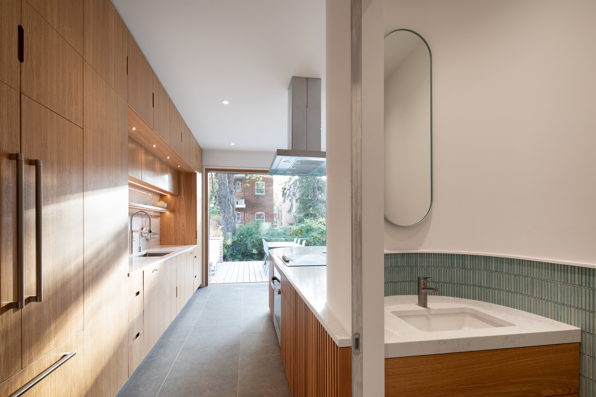 Discreetly tucked away, this minimalist powder room features porcelain tile flooring and curved detailing that echo the kitchen’s refined material palette.