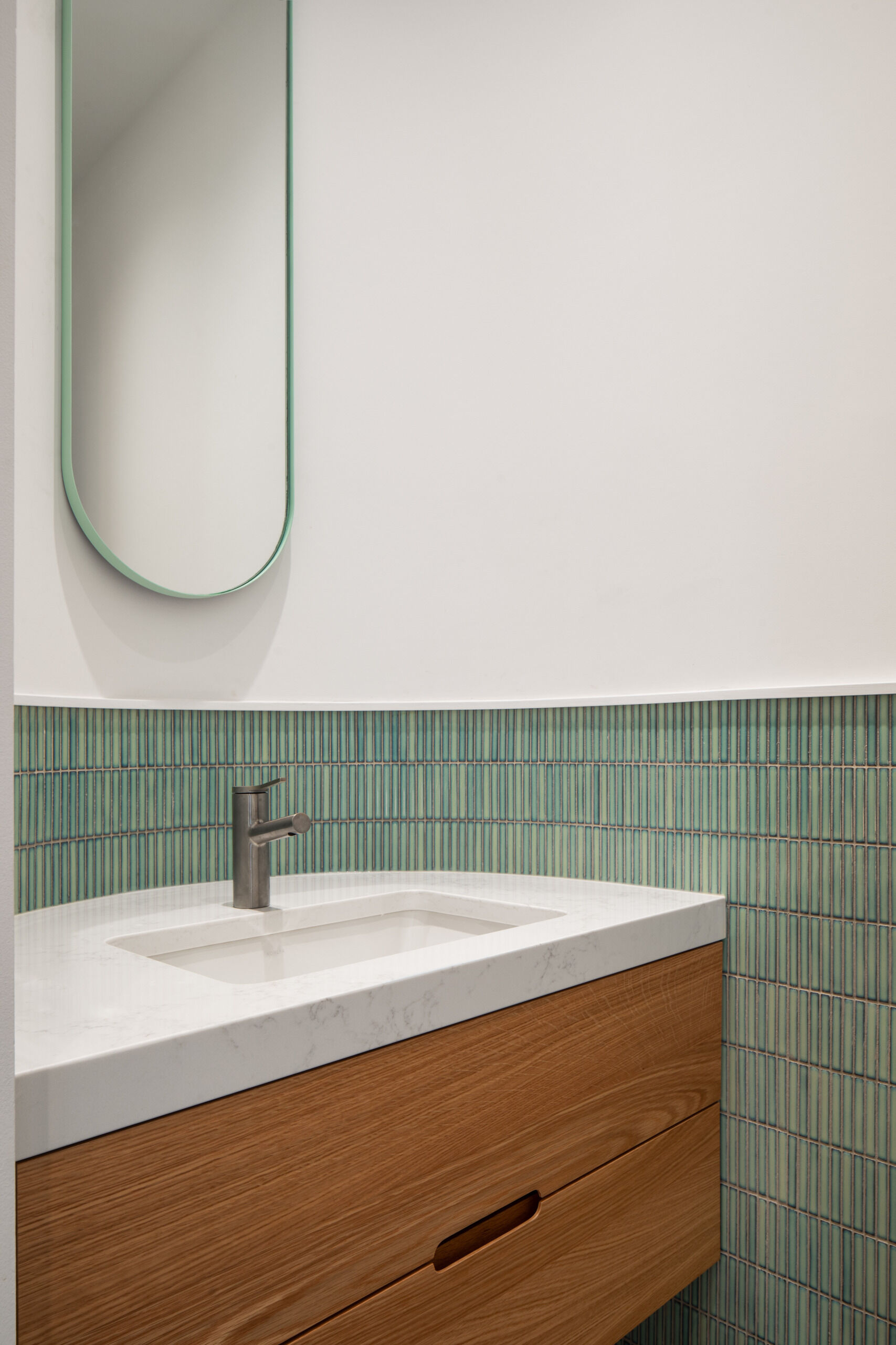Discreetly tucked away, this minimalist powder room features porcelain tile flooring and curved detailing that echo the kitchen’s refined material palette.