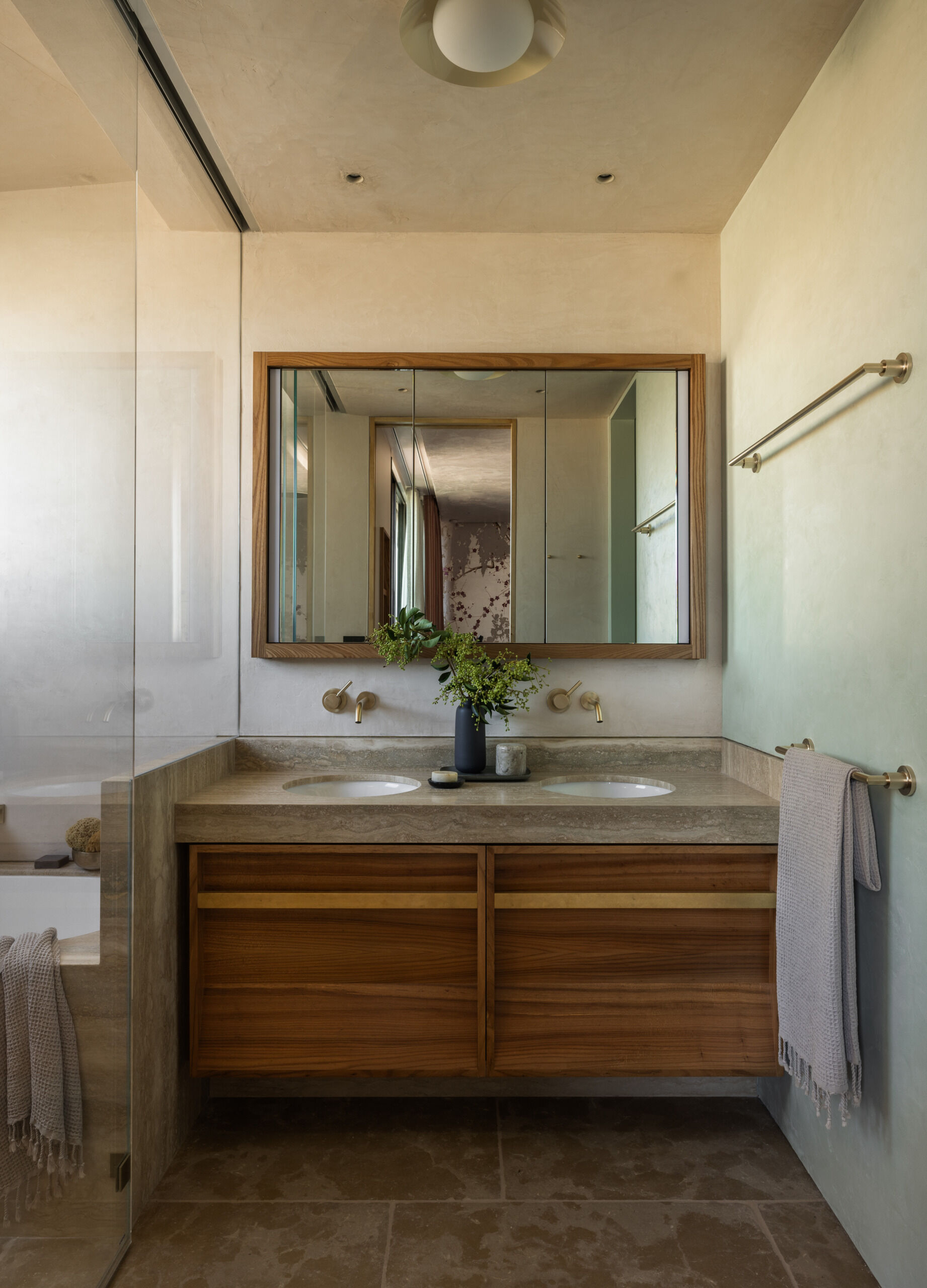 This primary bathroom carries over the home's theme of time-worn elegance, with a palette inspired by Italian ceramic beach tiles. A vanity wrapped in Zak & Fox wallcoverings and paired with a Nickey Kehoe stool reinforces the custom, collected feel.