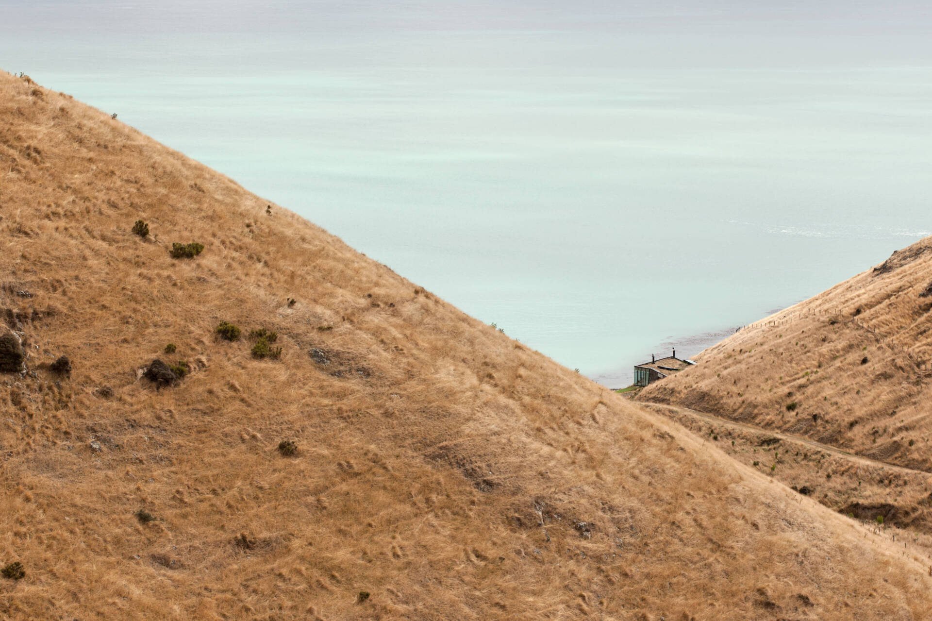 A stone cottage built using local rock, concrete, and timber to disappear into the landscape. The green roof and interlocking plan create a seamless connection with sea and sky.