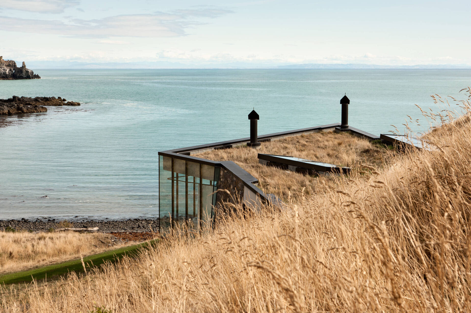 A stone cottage built using local rock, concrete, and timber to disappear into the landscape. The green roof and interlocking plan create a seamless connection with sea and sky.