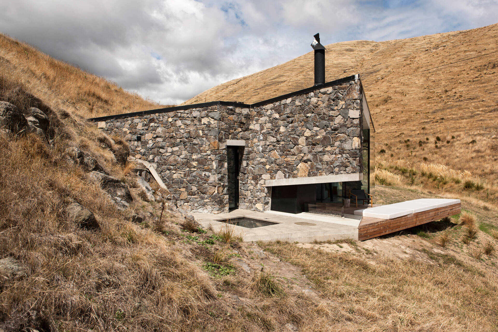 A stone cottage built using local rock, concrete, and timber to disappear into the landscape. The green roof and interlocking plan create a seamless connection with sea and sky.