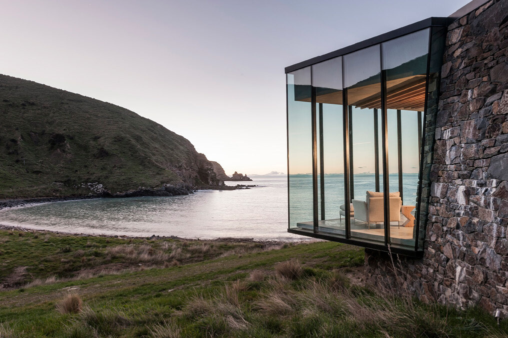 A stone cottage built using local rock, concrete, and timber to disappear into the landscape. The green roof and interlocking plan create a seamless connection with sea and sky.