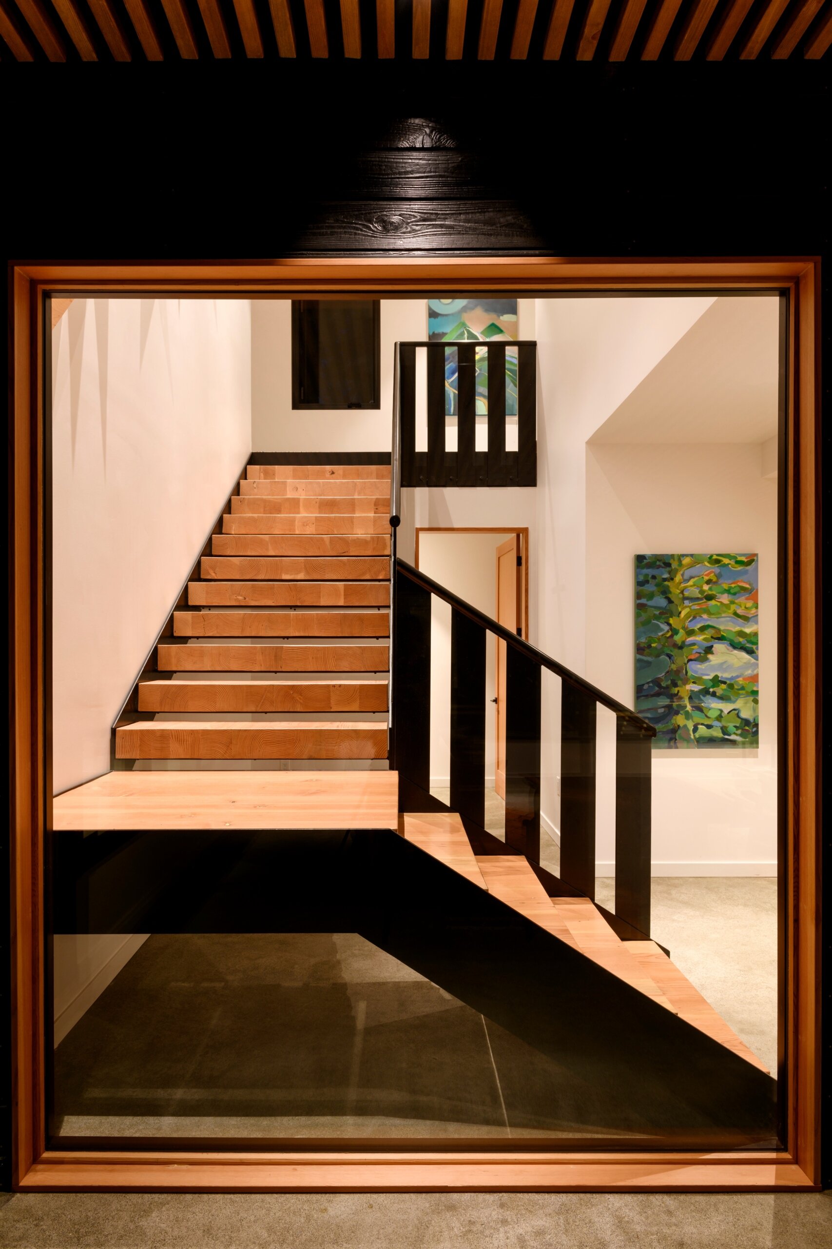 A minimal stairwell with floating wood treads, black accents, and polished concrete—brightened by natural light and playful abstract art.