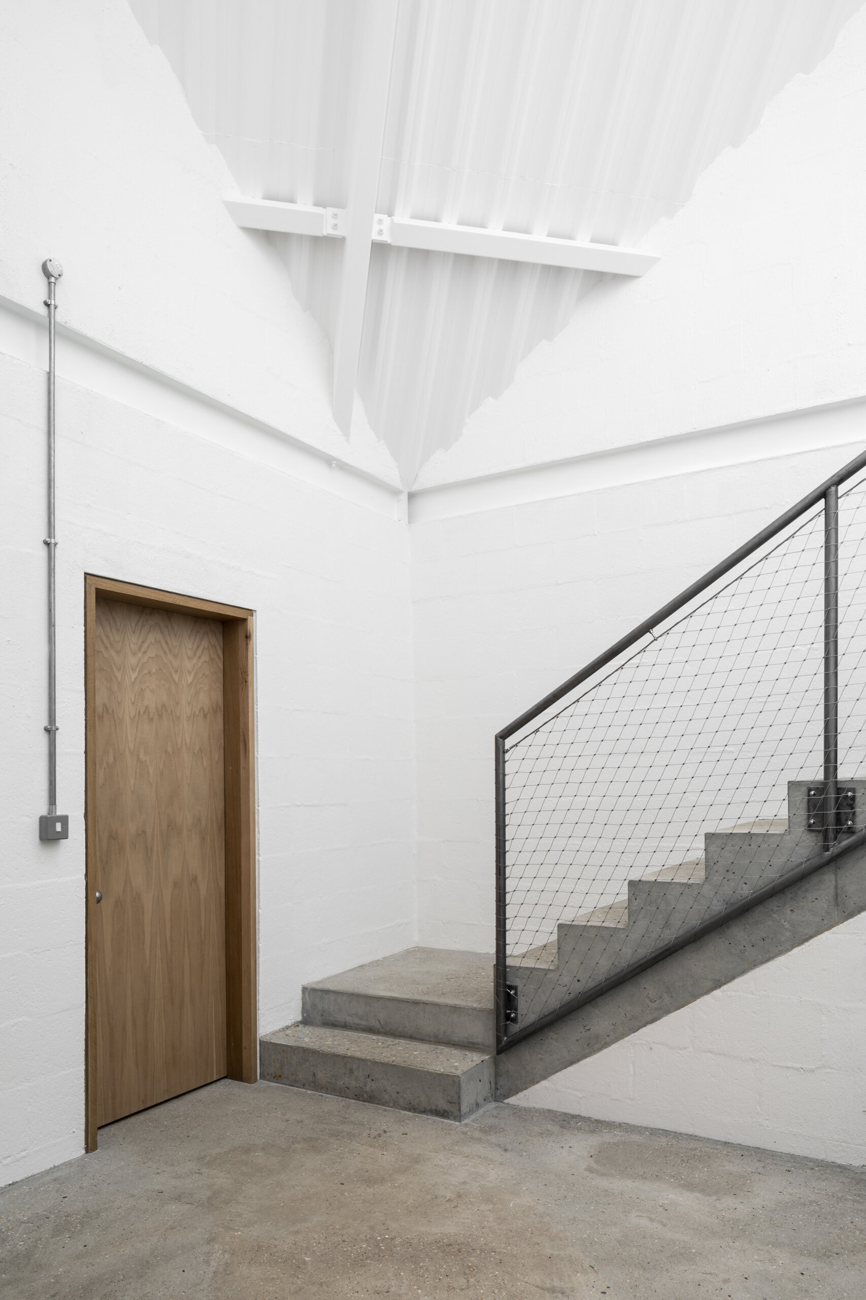 The staircase begins in a dramatic triple-height hall and leads through shadowy transitions, setting the rhythm for how the house unfolds.