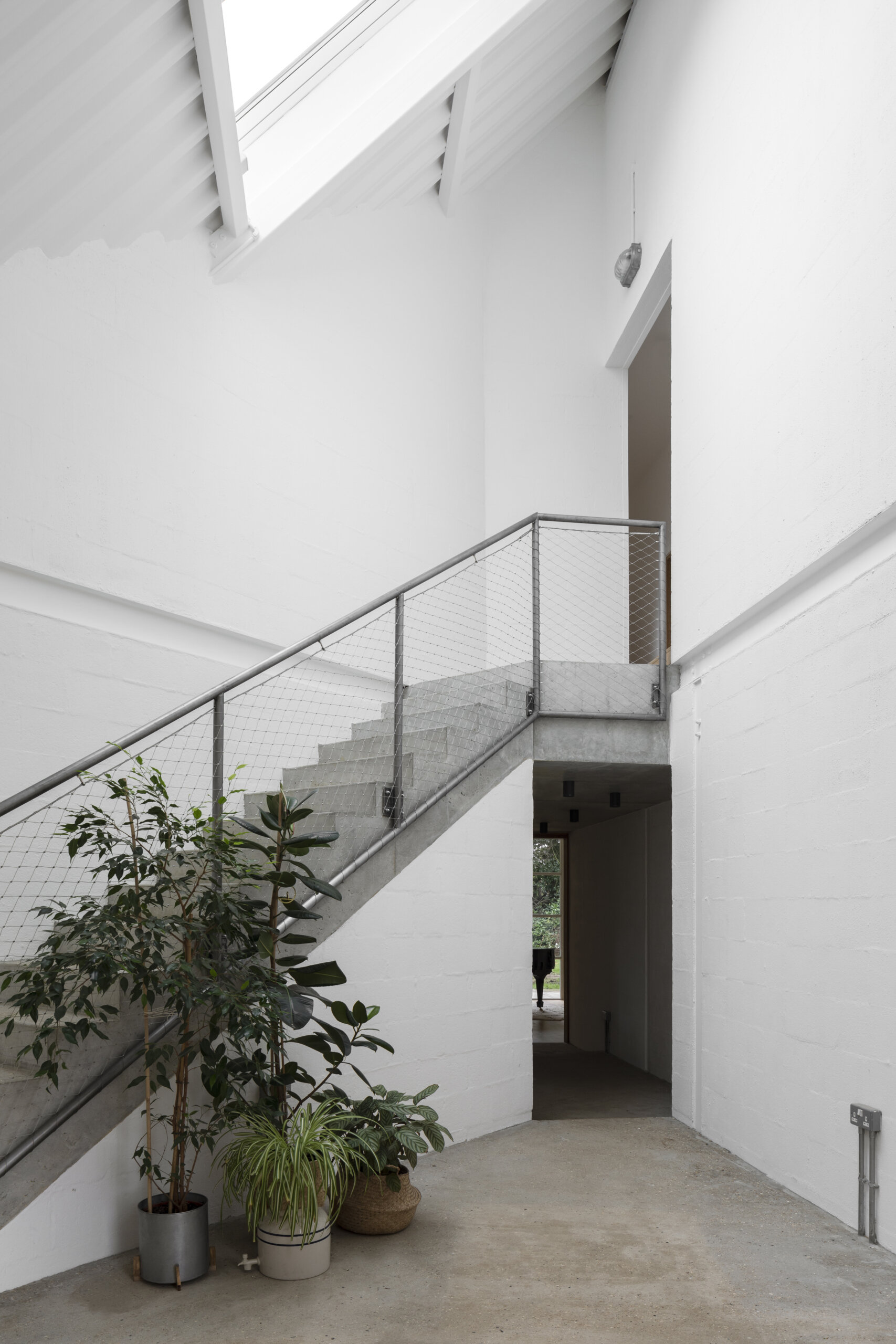 The staircase begins in a dramatic triple-height hall and leads through shadowy transitions, setting the rhythm for how the house unfolds.