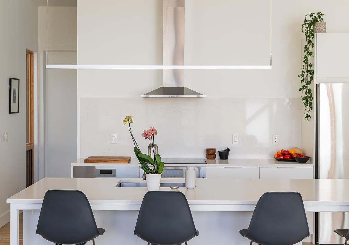 The kitchen features white IKEA cabinets and and island topped with durable quartz countertops, combining practicality with minimalist style. A glass slider connects the kitchen to a covered deck that overlooks the creek, allowing meals to extend outdoors and inviting fresh air and nature inside.