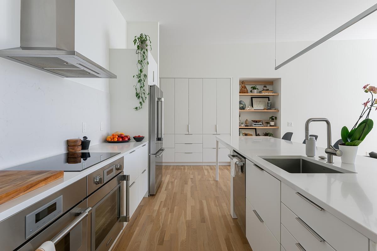The kitchen features white IKEA cabinets and and island topped with durable quartz countertops, combining practicality with minimalist style. A glass slider connects the kitchen to a covered deck that overlooks the creek, allowing meals to extend outdoors and inviting fresh air and nature inside.