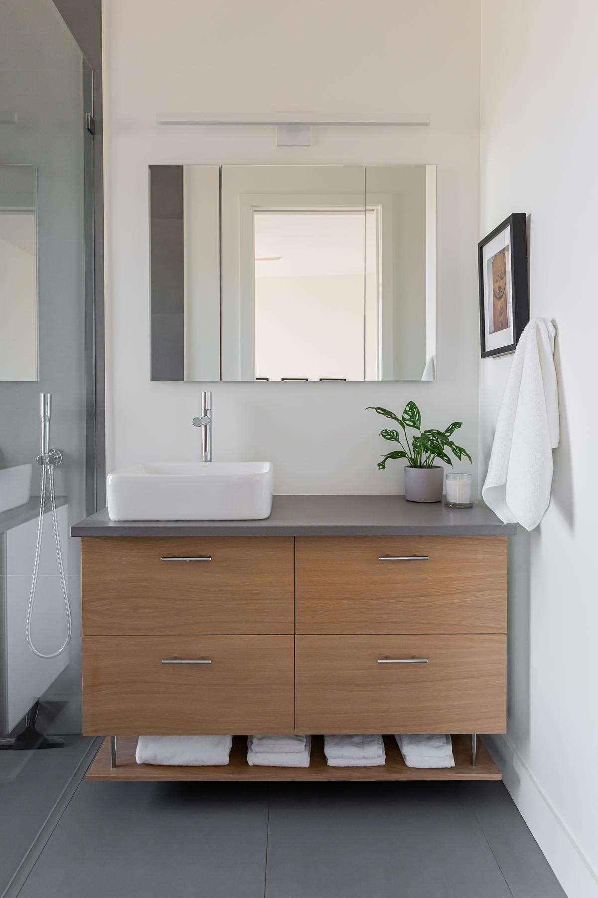A modern bathroom with a wood vanity, grey countertop, and white sink.
