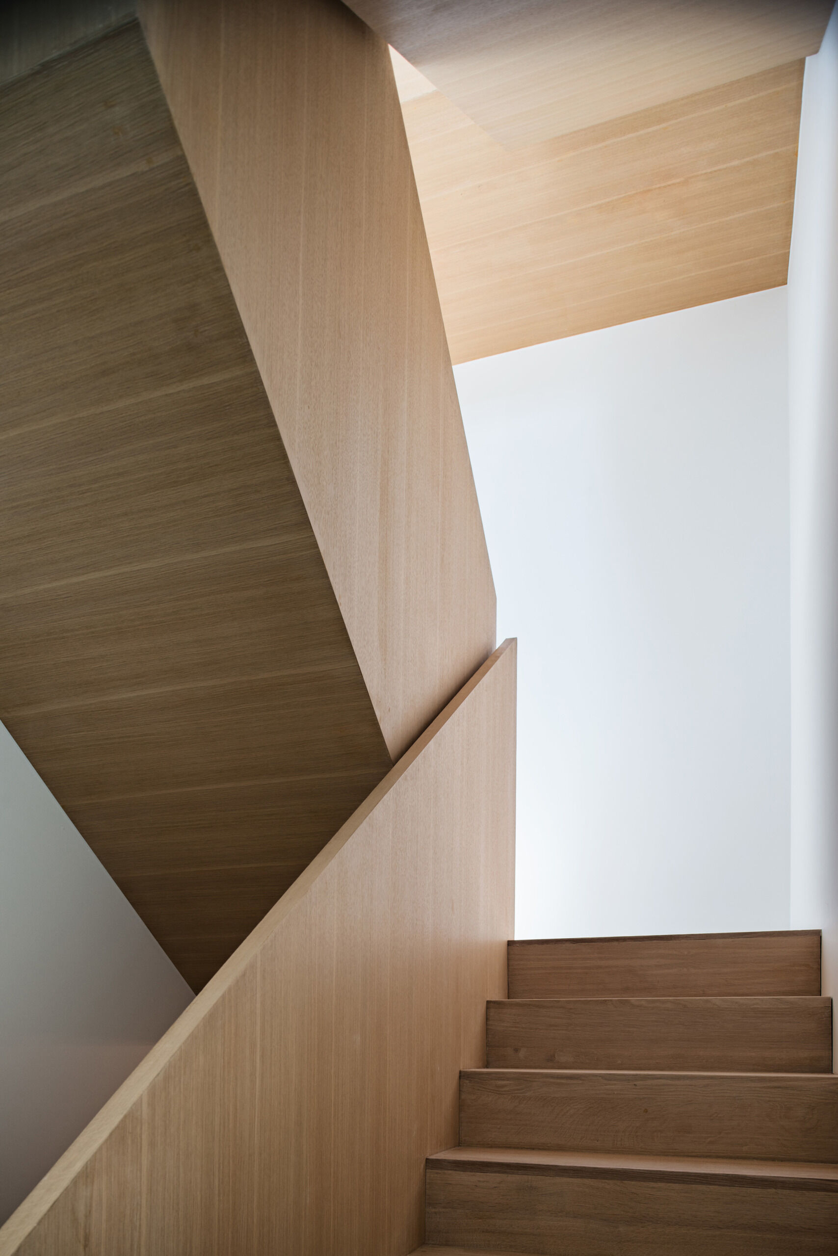 A sculpted wooden staircase anchors this Toronto home, showcasing warm craftsmanship by Tact Design Inc. It leads to a peaceful study and wrap-around terrace above.
