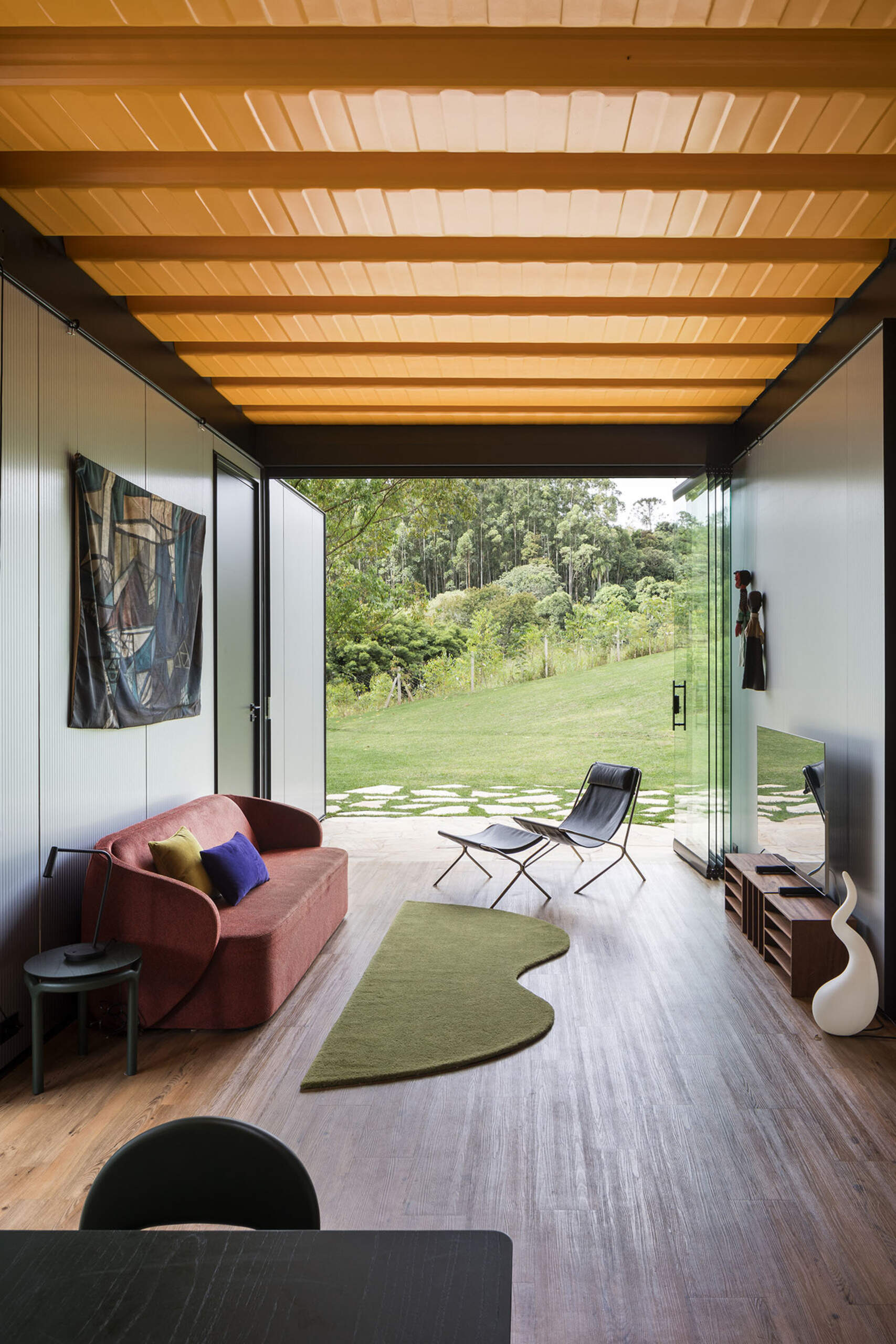 This cozy media room opens directly to nature. A sculptural sofa and playful green rug add warmth and style to this laid-back escape.