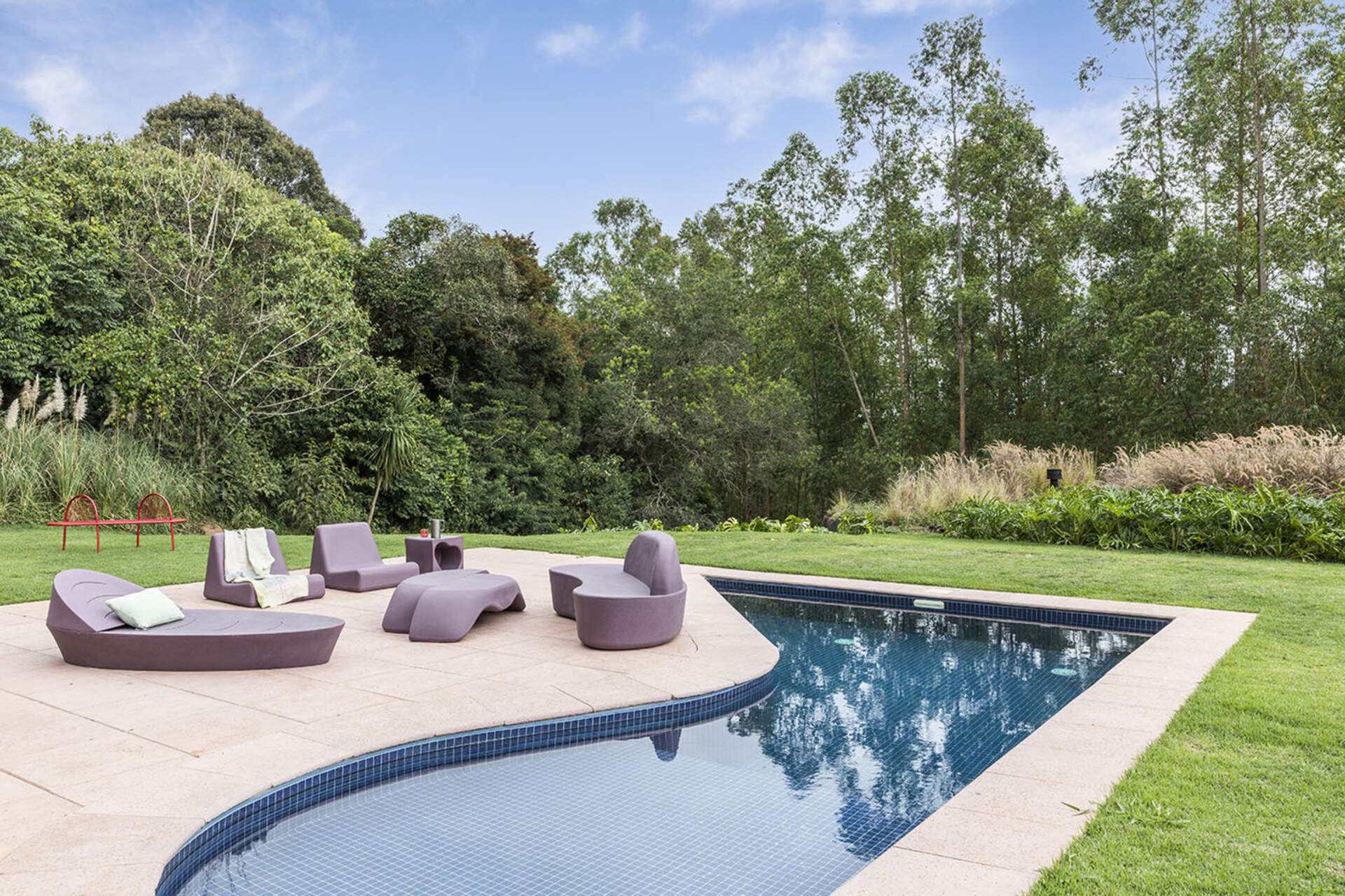A curved pool anchors the garden with its sculptural form. Designed for play and relaxation, it echoes the home’s fluid lines and bold personality.