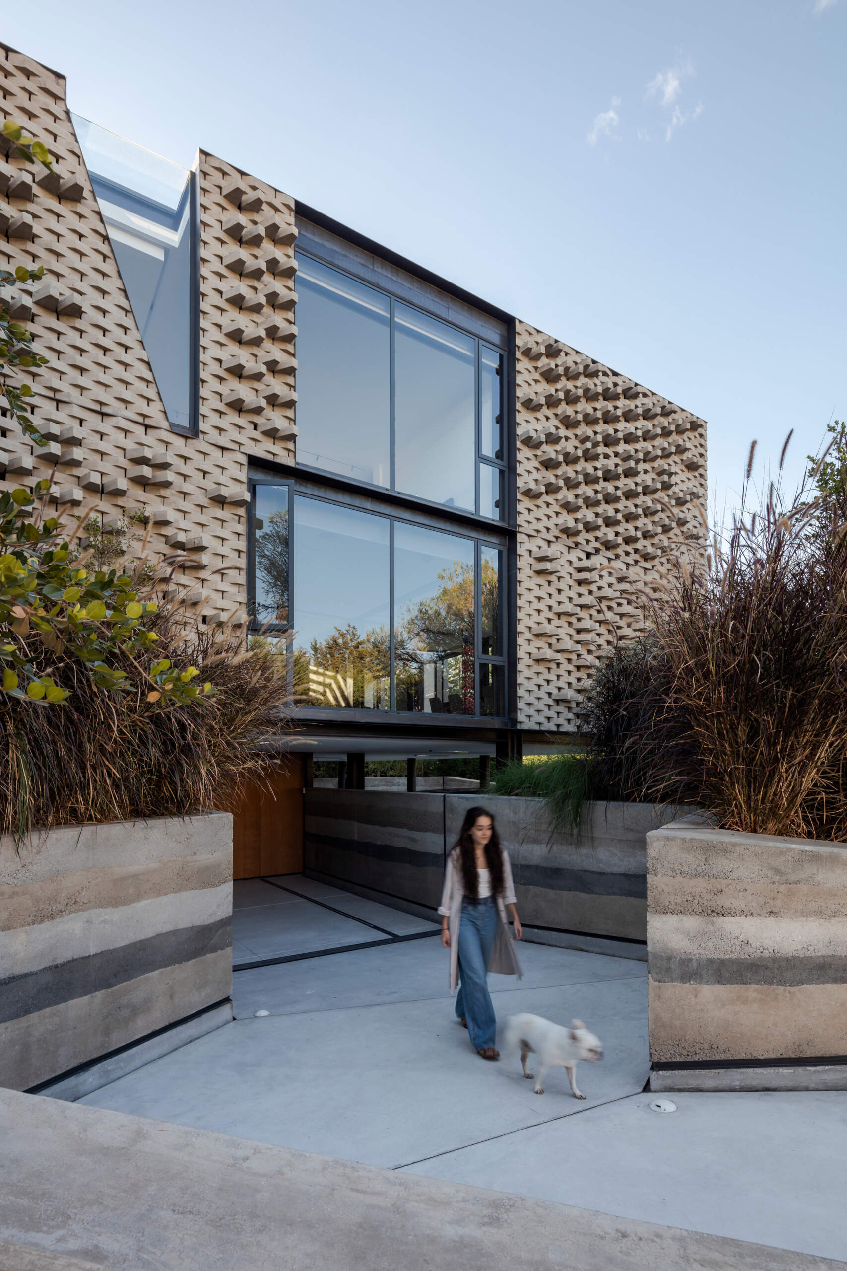 The entry path is carved through sculpted mounds of native plants, leading to a monumental rammed earth wall. It feels like a rediscovered trail through the Andes.