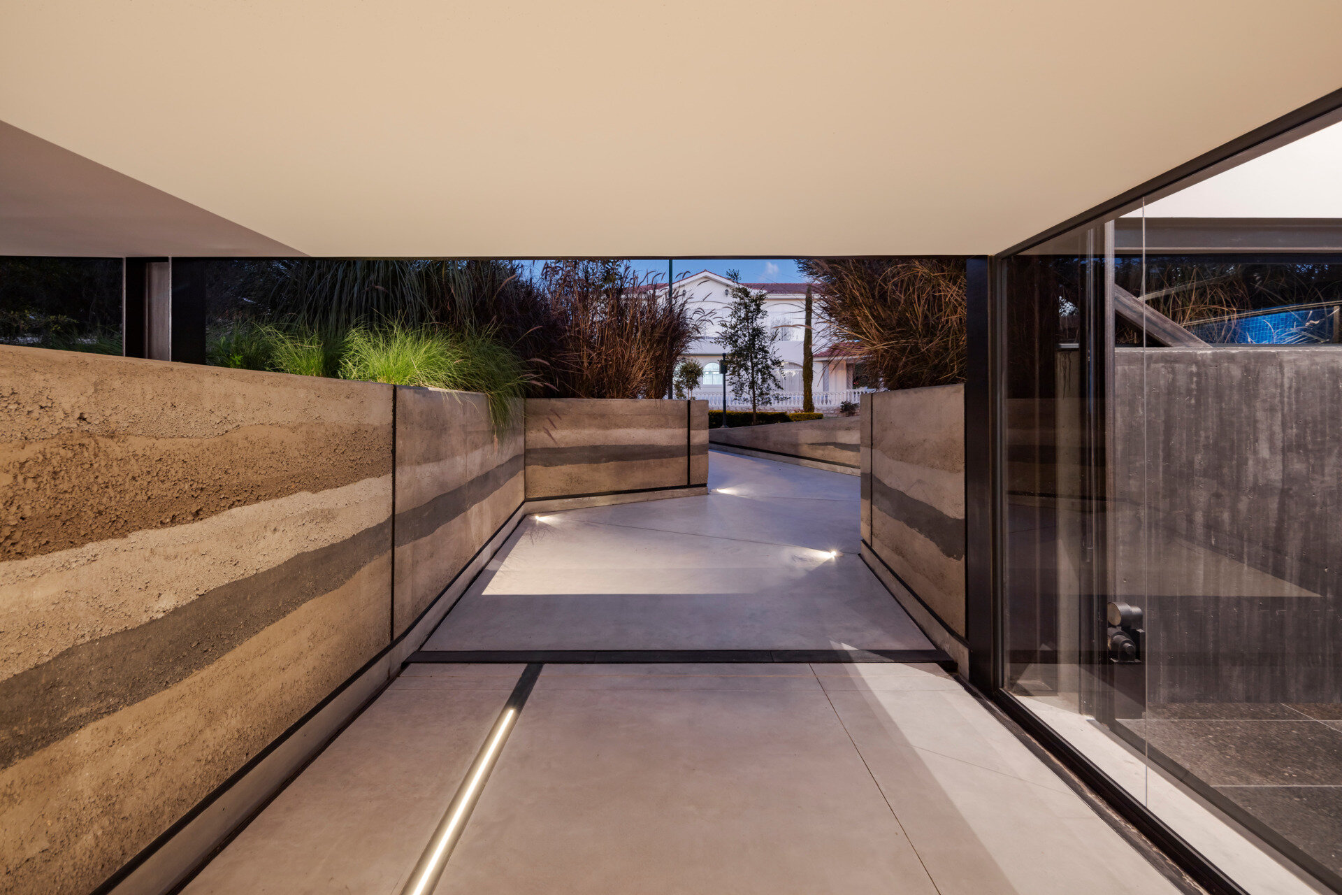 The entry path is carved through sculpted mounds of native plants, leading to a monumental rammed earth wall. It feels like a rediscovered trail through the Andes.