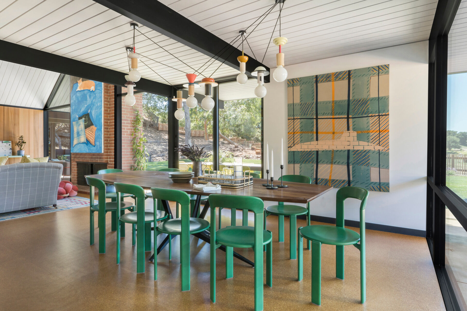 The dining area continues the home's organic palette, with cork flooring, natural stone, and warm wood tones. A set of green chairs introduces a playful pop of color, bringing freshness to the refined material mix.
