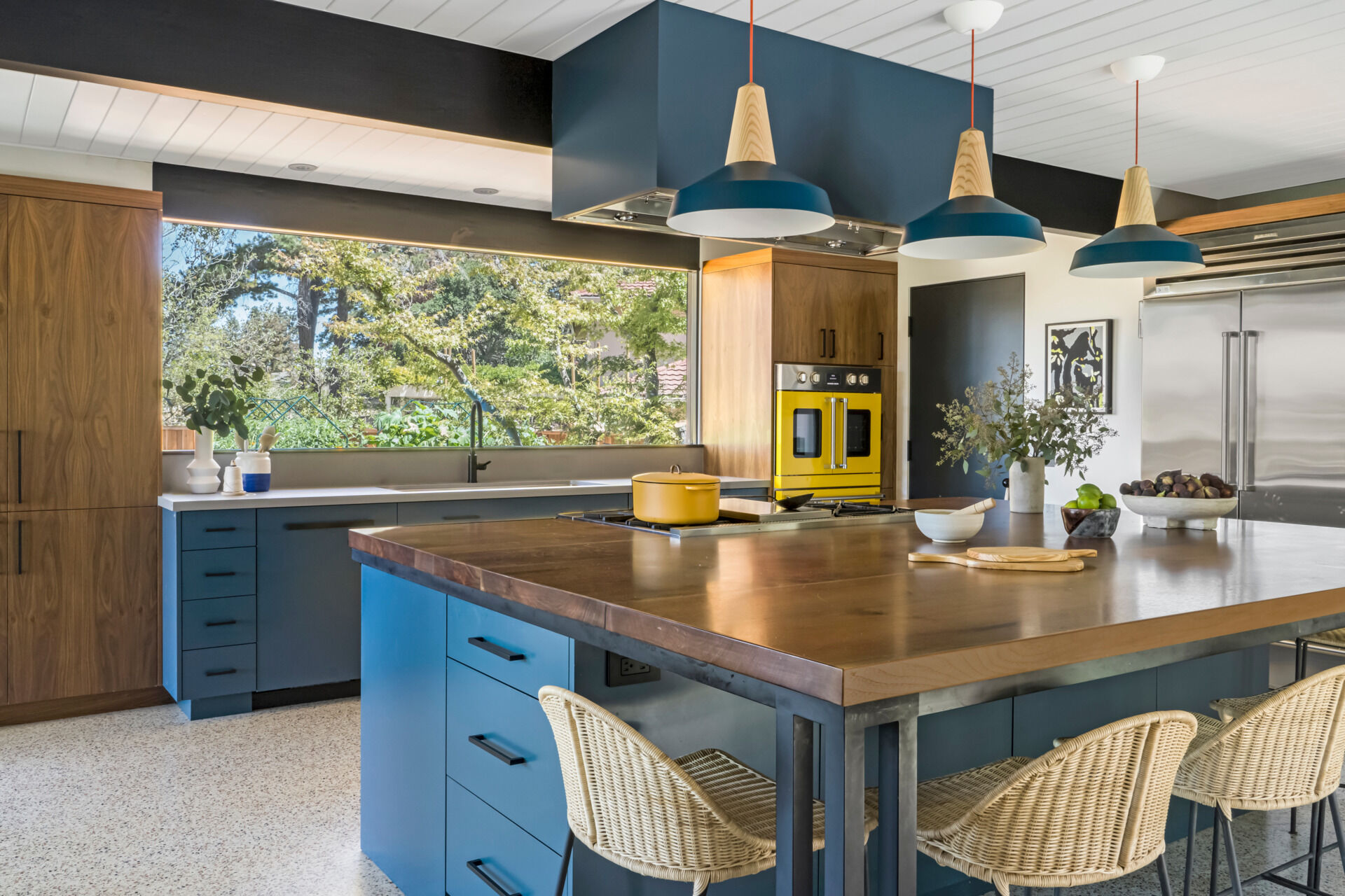 Color ties the house together, with blue, coral, and yellow tones appearing throughout. In the sunlit kitchen, cabinetry painted in Farrow & Ball's Hague Blue No. 30 anchors the room. A central island, topped with black walnut and supported by custom steel legs, blends function with elegance. Nearby, the home office area echoes the color scheme, creating continuity in daily-use spaces.