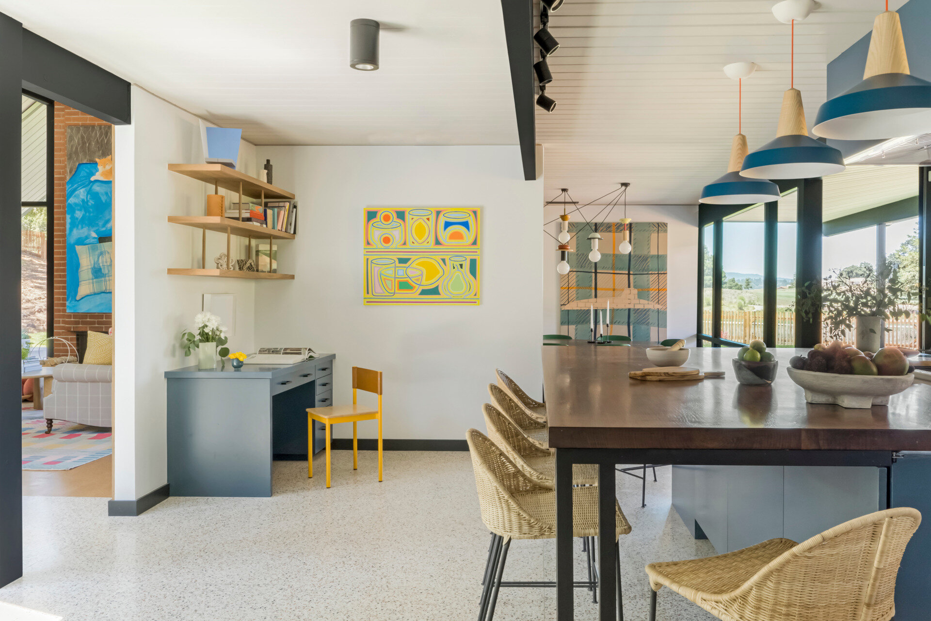 Color ties the house together, with blue, coral, and yellow tones appearing throughout. In the sunlit kitchen, cabinetry painted in Farrow & Ball's Hague Blue No. 30 anchors the room. A central island, topped with black walnut and supported by custom steel legs, blends function with elegance. Nearby, the home office area echoes the color scheme, creating continuity in daily-use spaces.